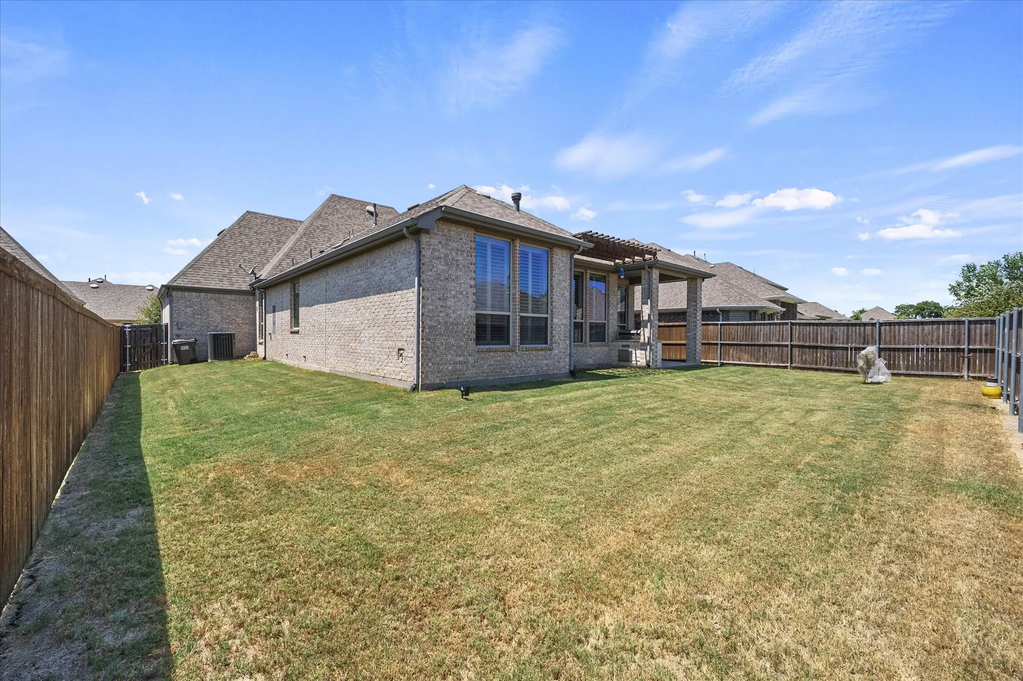 Expansive grassy yard with full privacy fencing, brick exterior, and covered patio