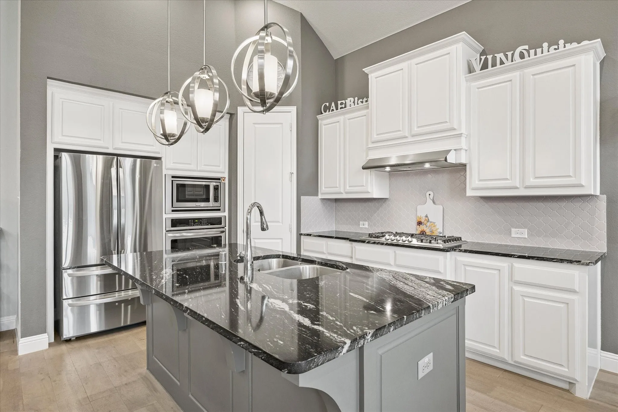 Kitchen featuring a center island with a sink, white cabinetry, stainless steel appliances, a gas cooktop, and contemporary pendant lighting