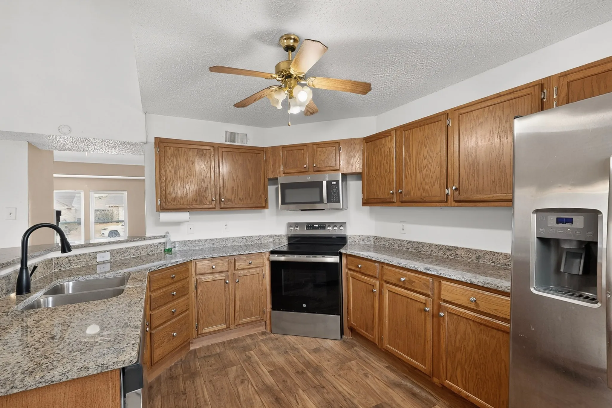 Kitchen featuring wood-finish flooring, granite countertops, stainless steel appliances, wood cabinetry, and a ceiling fan