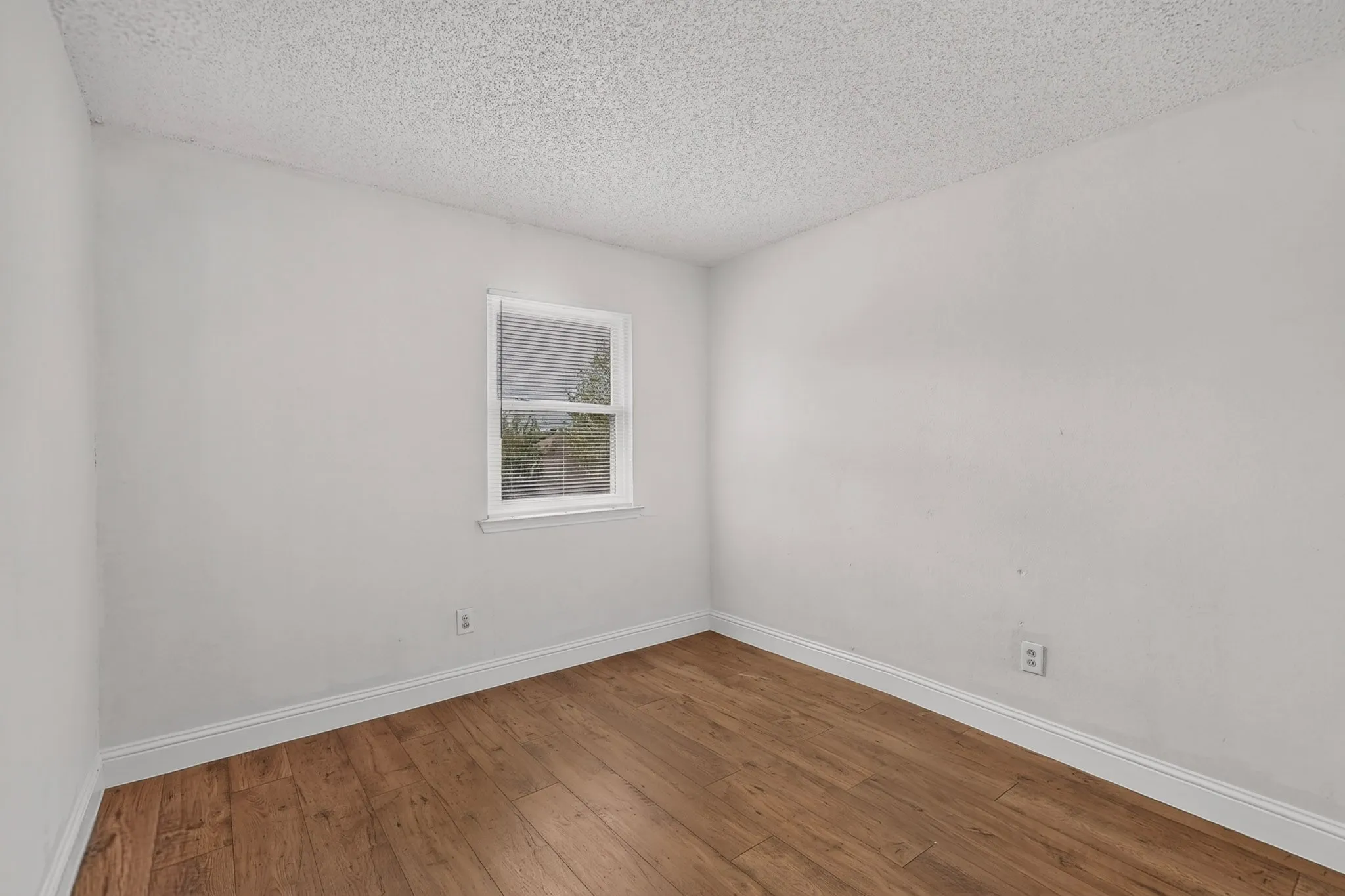 Wood-finish flooring, white trim, and a window with blinds