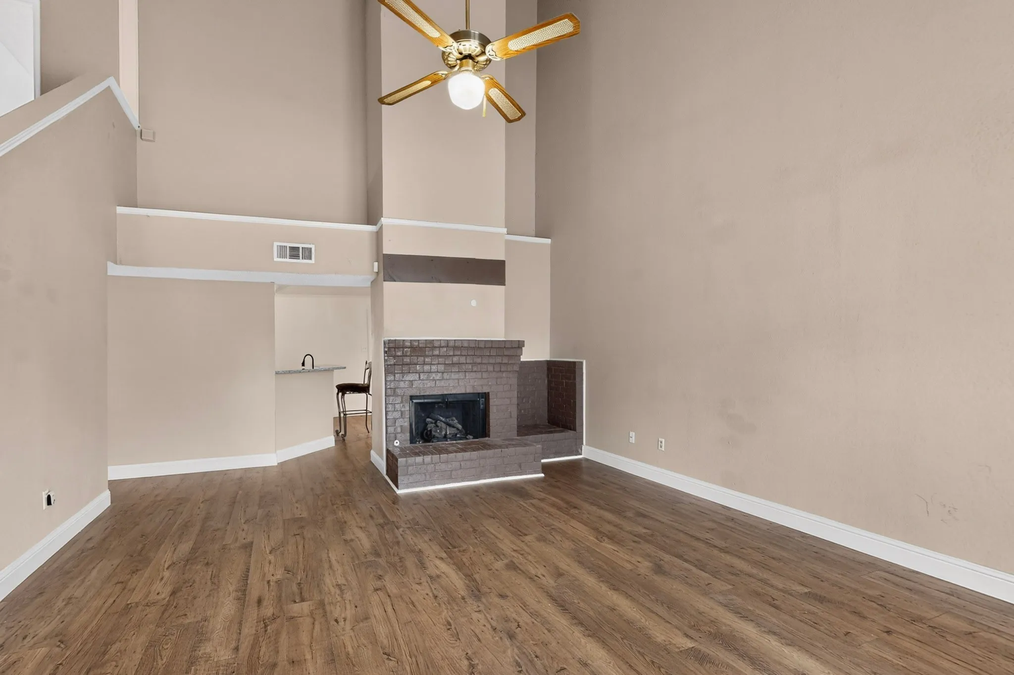 Vaulted ceilings, wood-finish flooring, brick-surround fireplace, and a ceiling fan