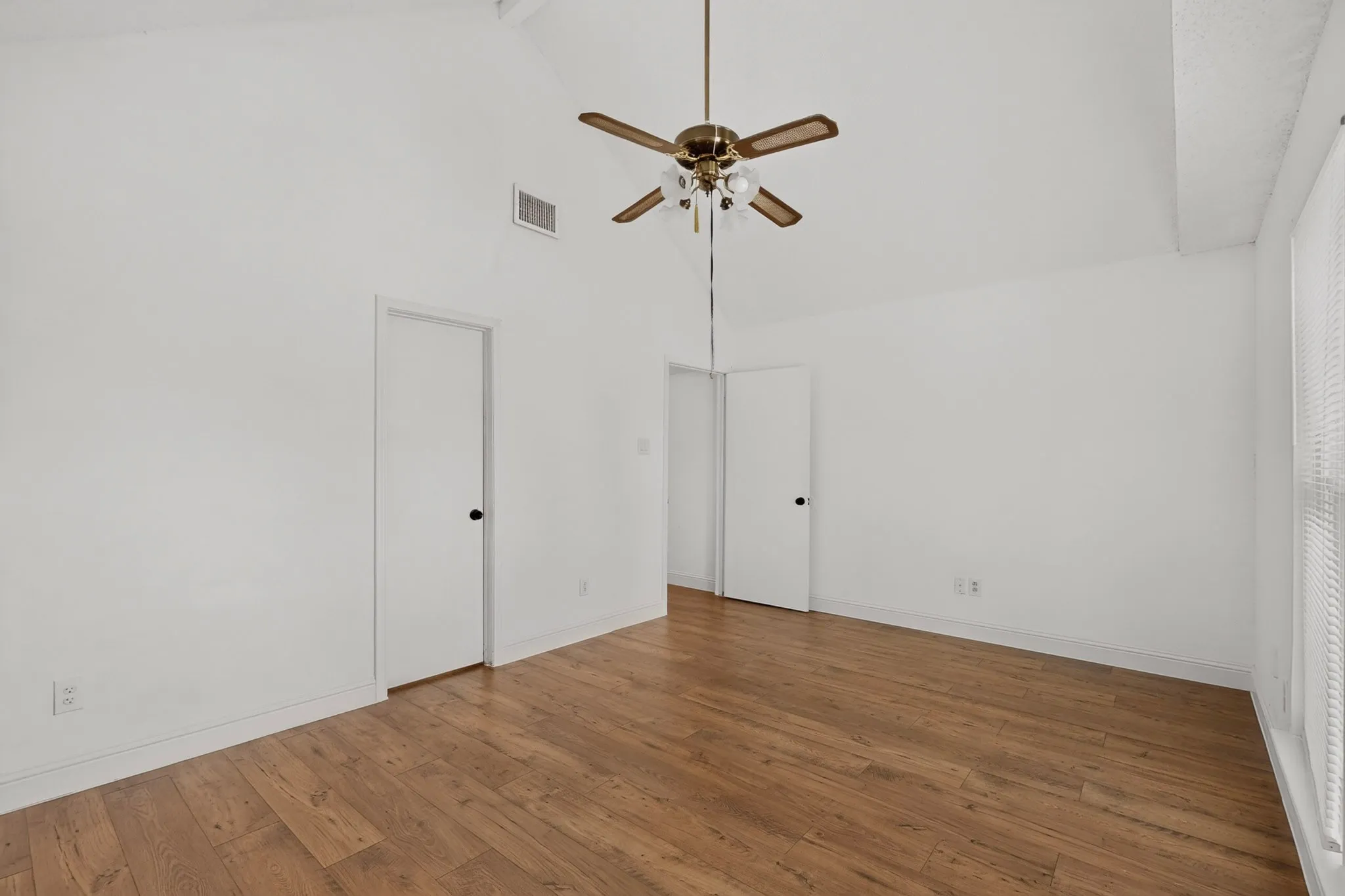 Vaulted ceiling, wood-finish flooring, ceiling fan with integrated lighting, white interior doors, and window with blinds