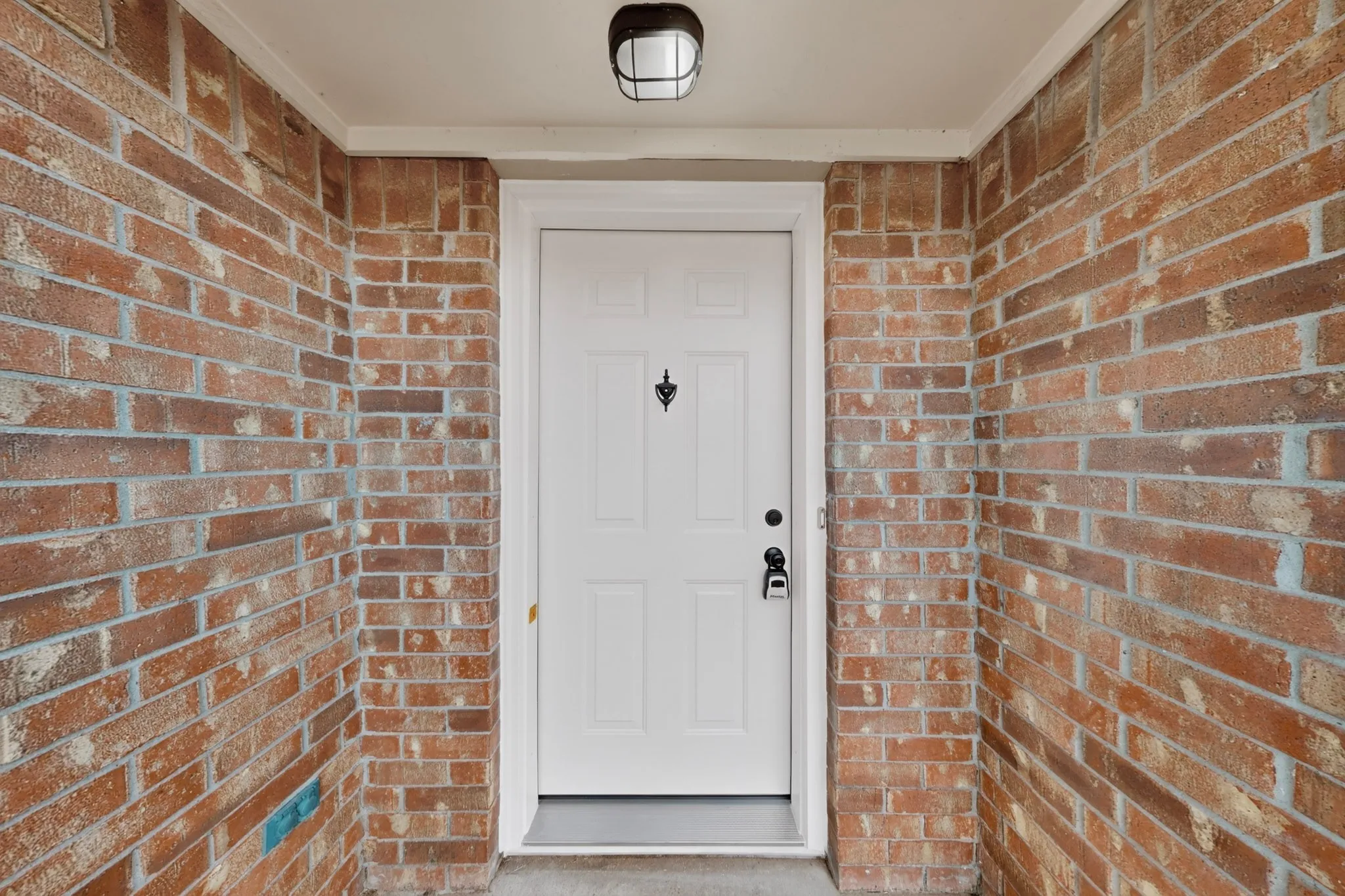 Brick exterior with a paneled white entry door, featuring a black door knocker and coordinating hardware
