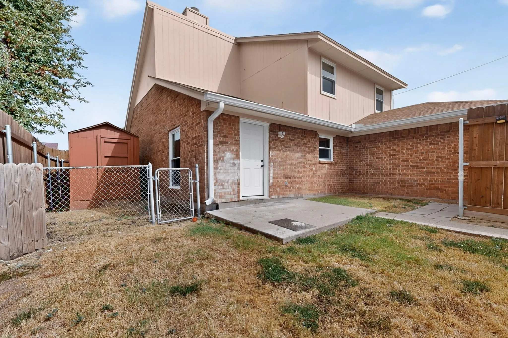 Brick exterior with a detached shed, chain link fencing, wooden privacy fencing, and a concrete patio