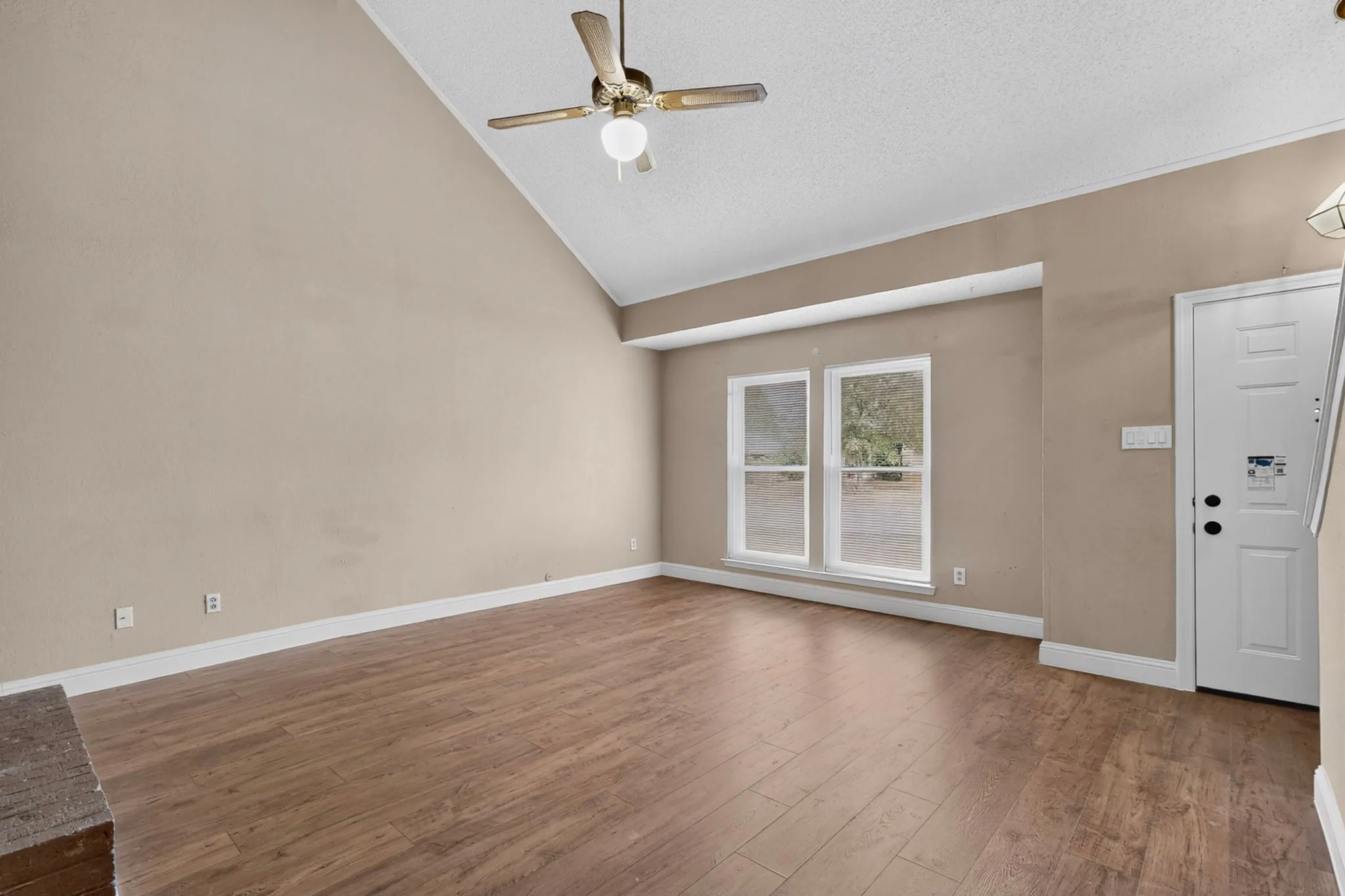 Vaulted ceiling with a ceiling fan, wood-finish flooring, and natural light from dual windows