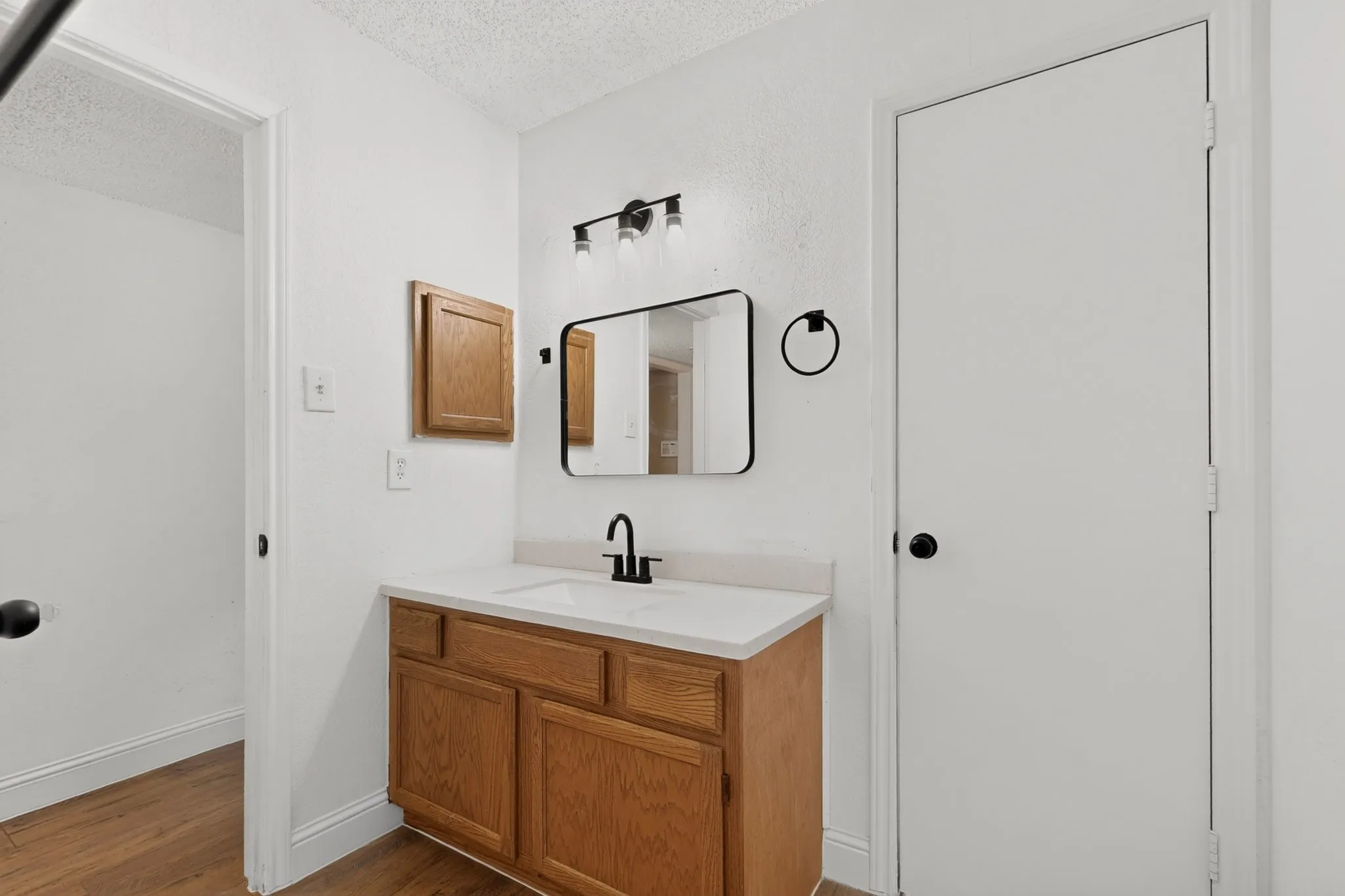 Wood-finish flooring, single vanity with a light-toned countertop, wood cabinetry, and a rectangular mirror