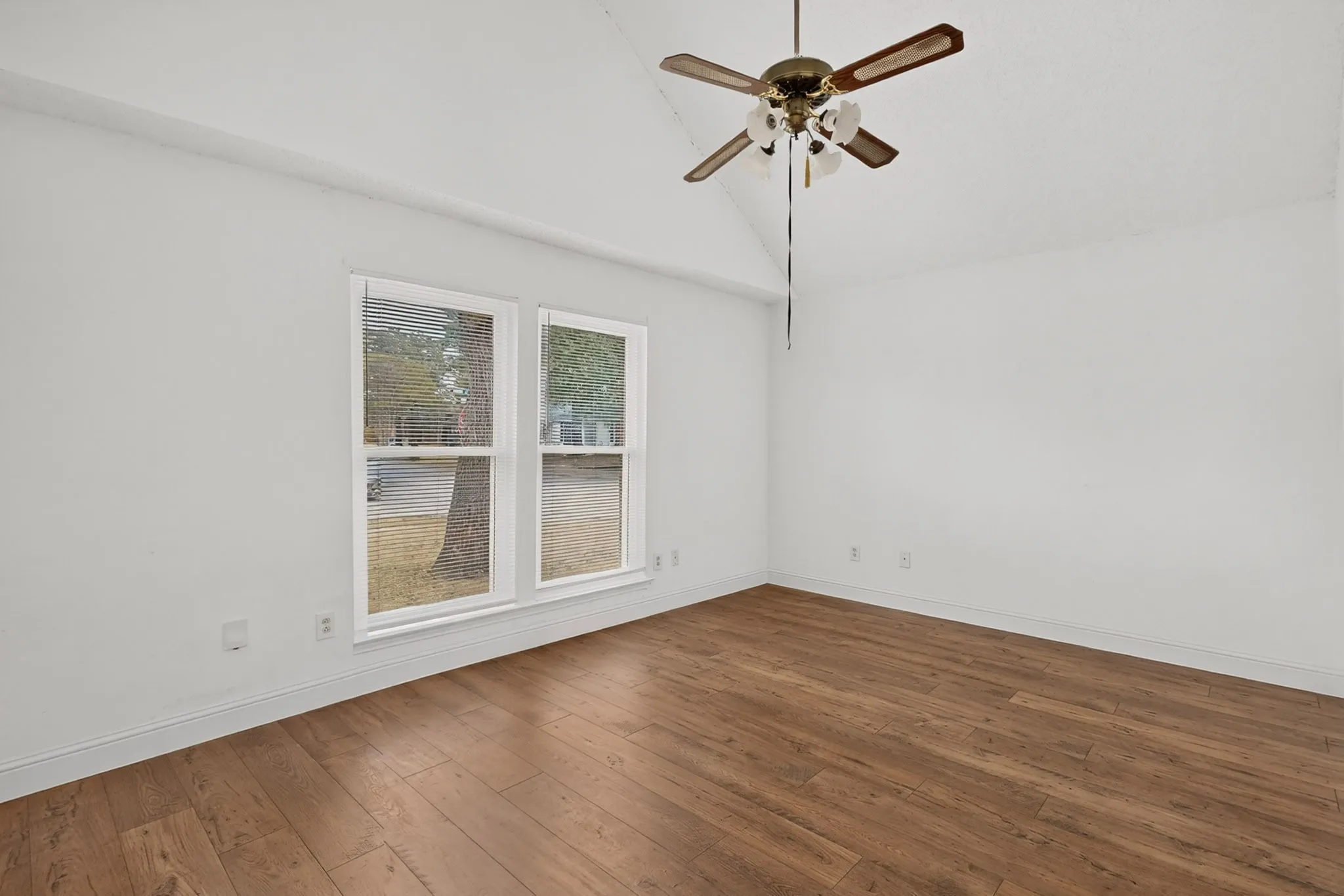 Vaulted ceiling with a ceiling fan, wood-finish flooring, and two windows