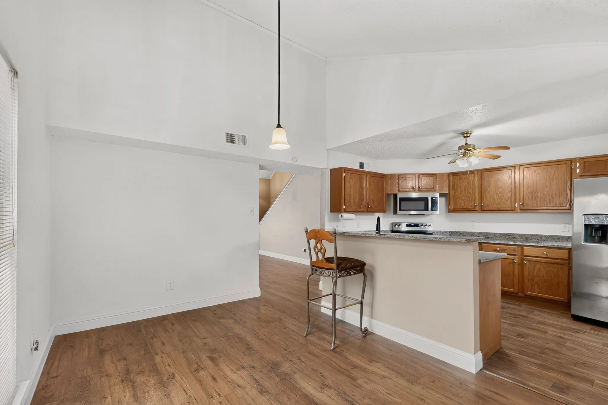 Vaulted ceiling, wood-finish flooring, kitchen with wood cabinetry, stainless steel appliances, and a breakfast bar