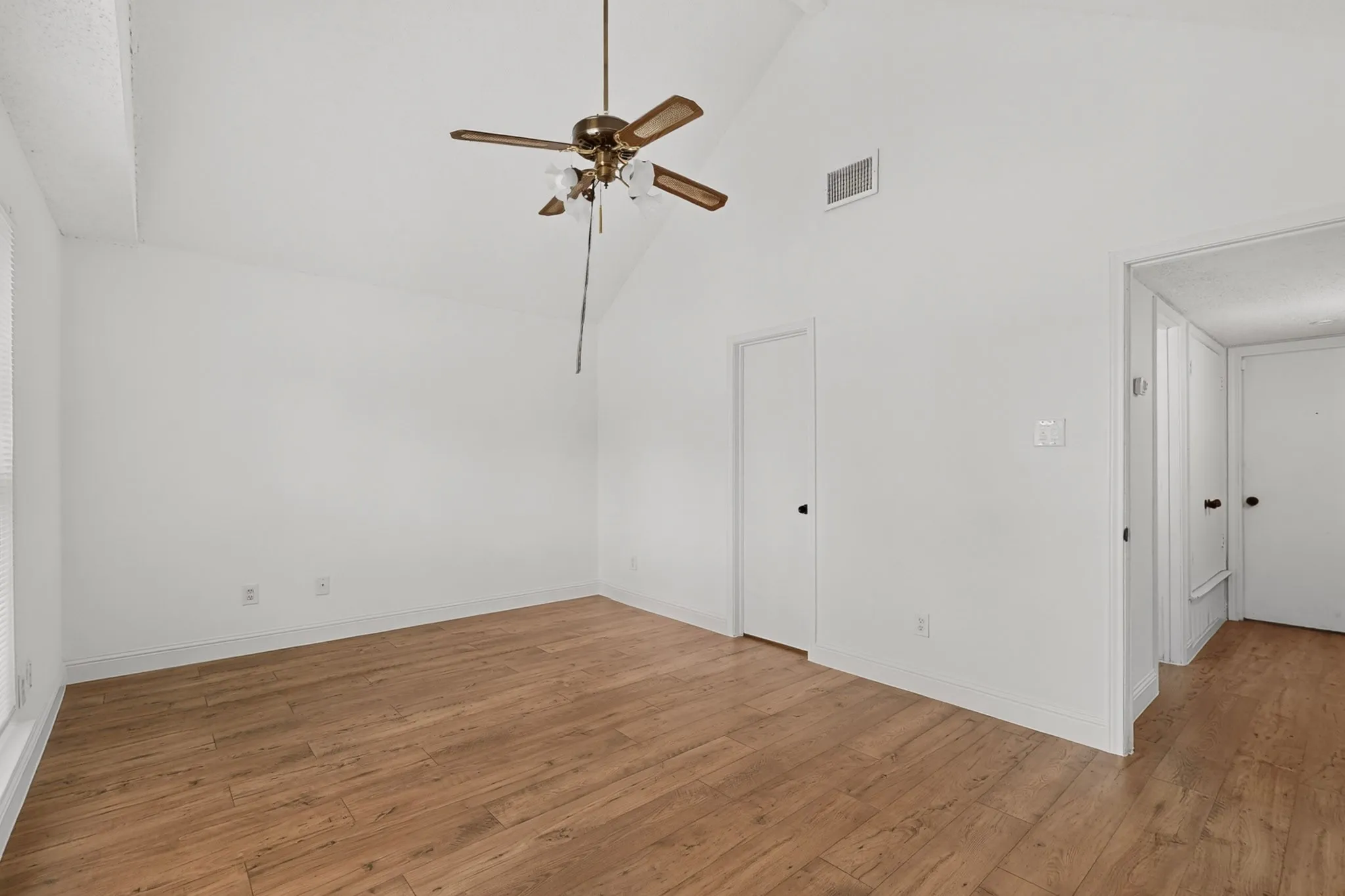 Vaulted ceiling with a ceiling fan, wood-finish flooring, and white walls