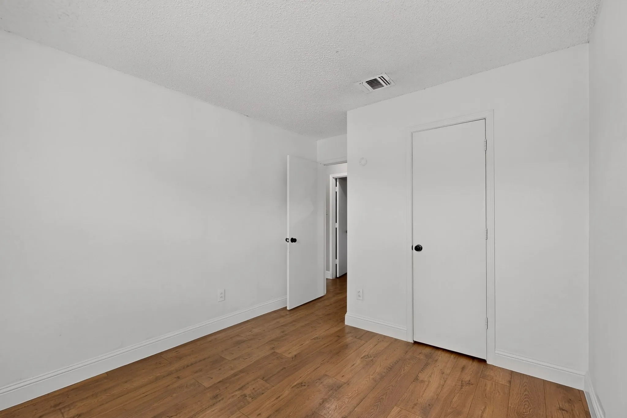 Wood-finish flooring with white baseboards, white walls, and white interior doors