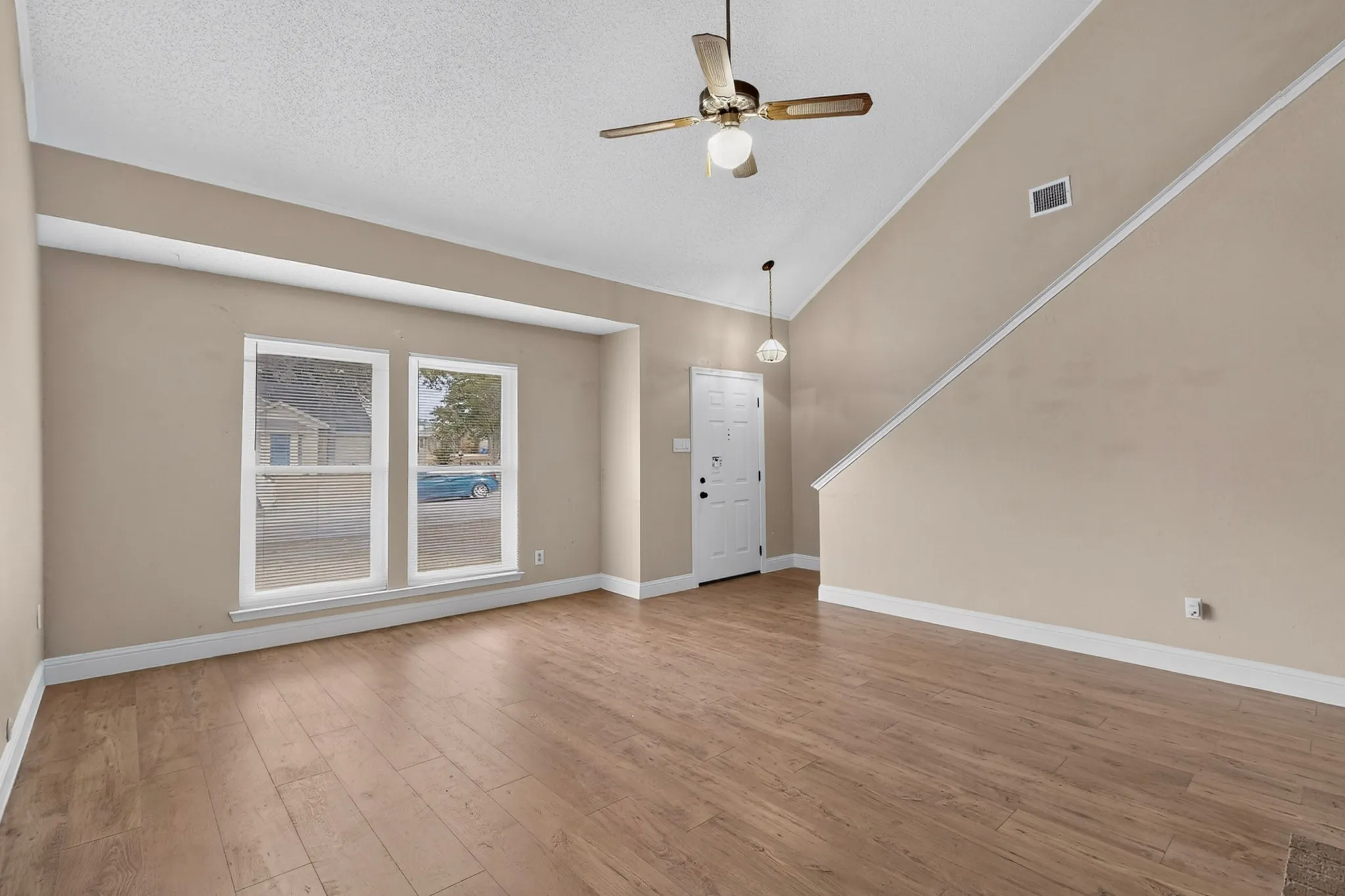 Vaulted ceiling with a ceiling fan, wood-finish flooring, and a white entry door with an overhead pendant light