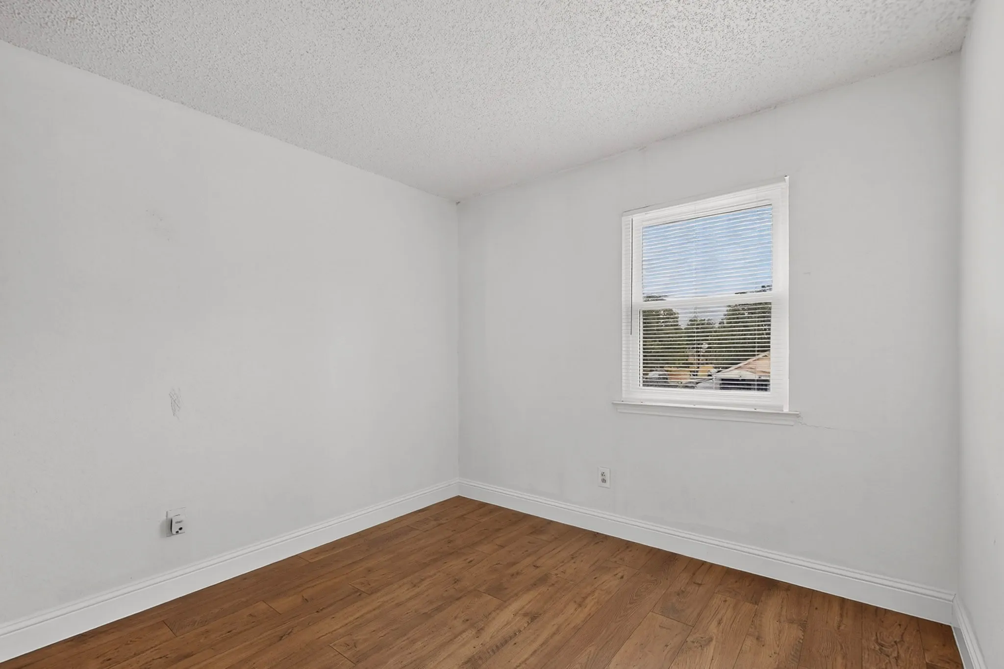 Wood-finish flooring, white walls, and a window with blinds