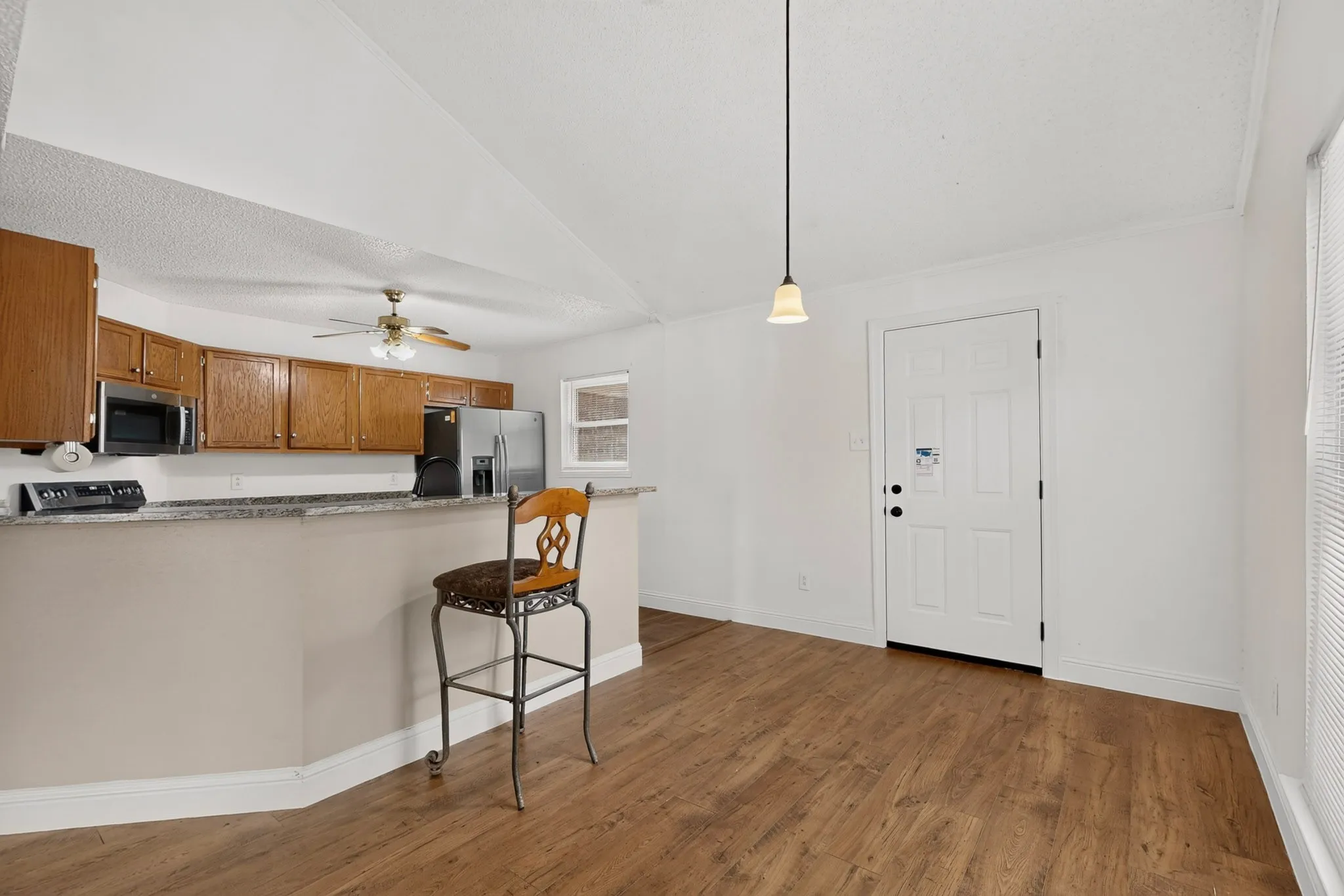 Kitchen area featuring wood cabinetry, stainless steel appliances, and a breakfast bar with a stone-finish countertop