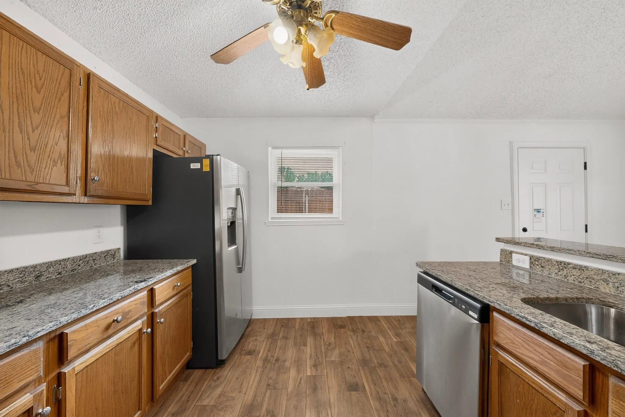 Kitchen featuring wood-finish flooring, wood cabinetry, stone countertops, and stainless steel appliances