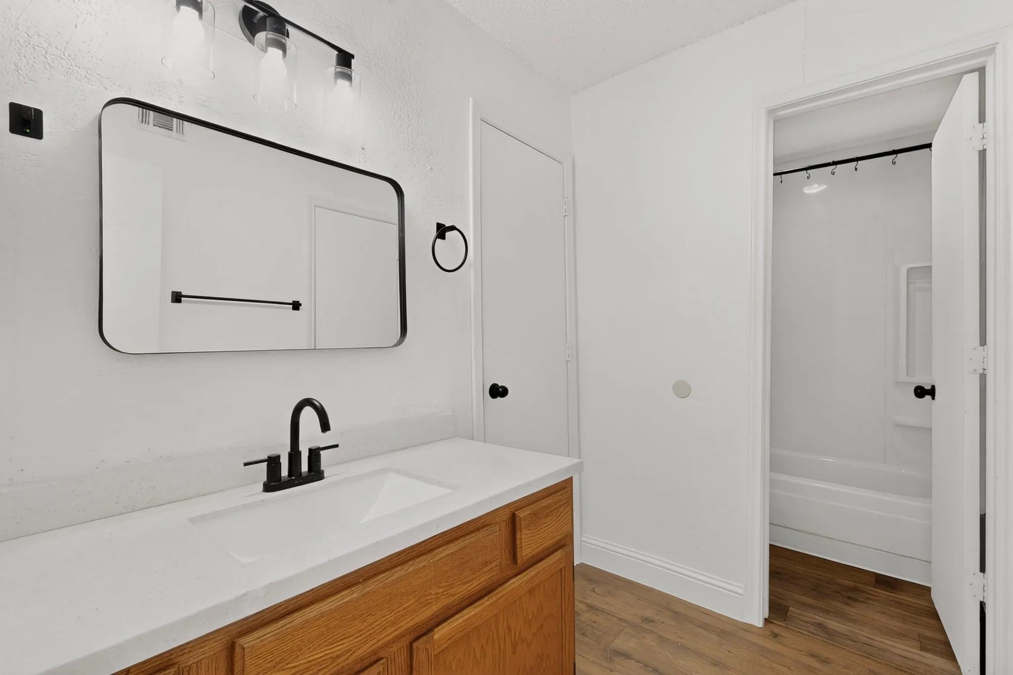 Bathroom featuring wood-finish flooring, a wood vanity, white countertop with an integrated sink, a rectangular mirror, and a shower-tub combination