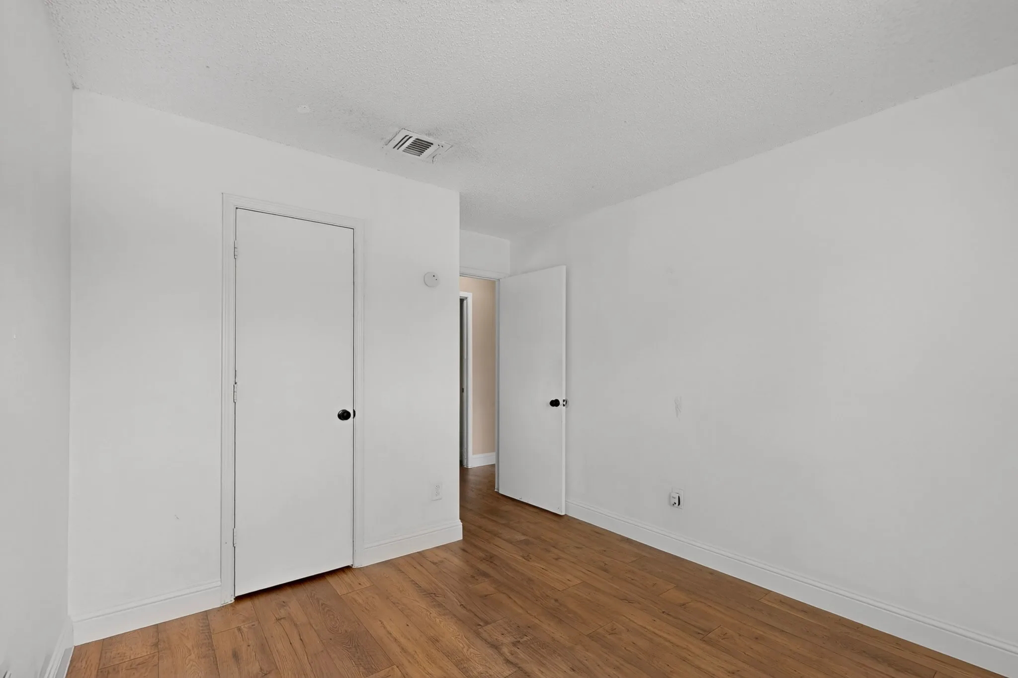 Wood-finish flooring with white baseboards, white walls, and white doors with dark hardware