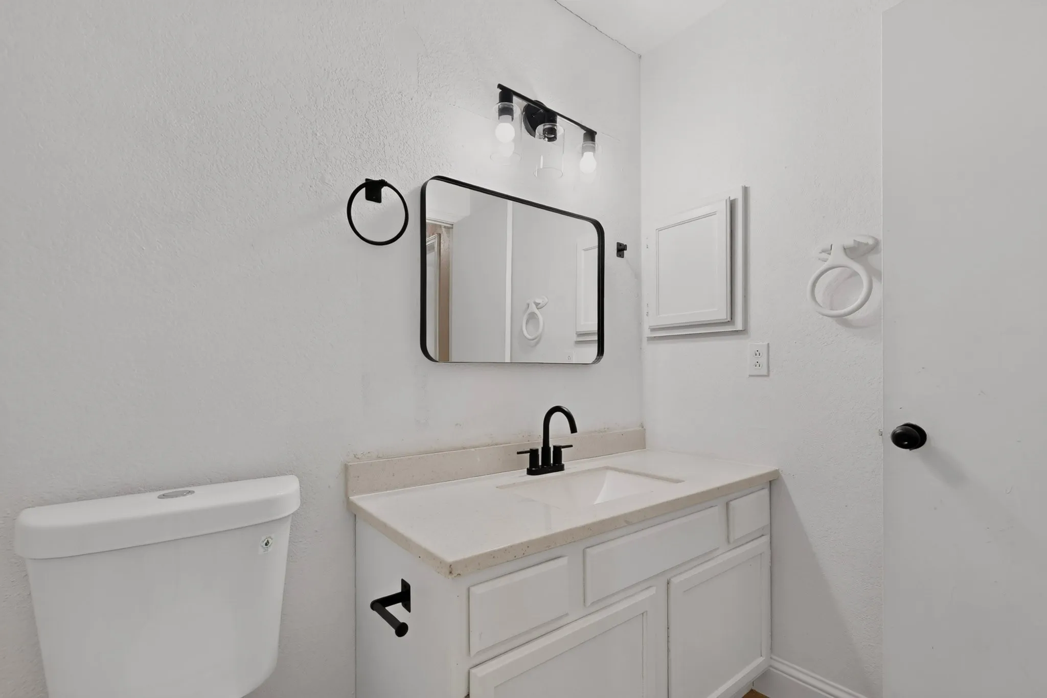 White vanity with a neutral countertop and integrated sink, matte black faucet, and rectangular mirror with a black frame