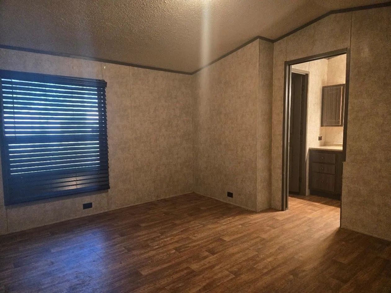 Wood-finish flooring with a neutral wall paneling and dark window blinds