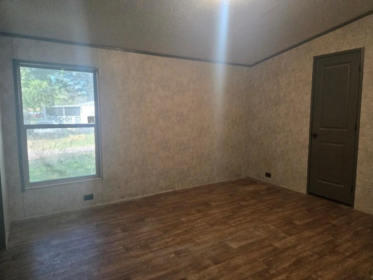 Wood-finish flooring with a neutral wall finish, a single window, and a paneled door