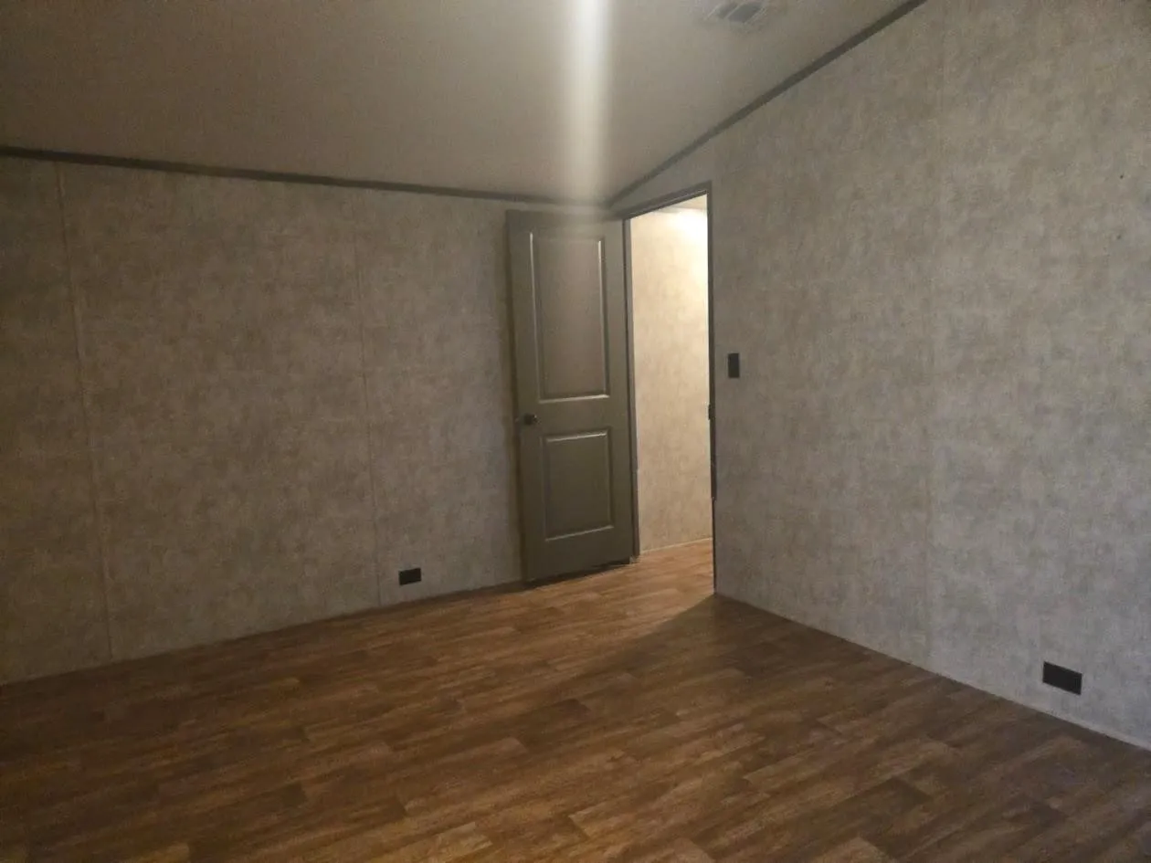 Wood-finish flooring with neutral-toned wall paneling, solid interior door, and ceiling-mounted lighting