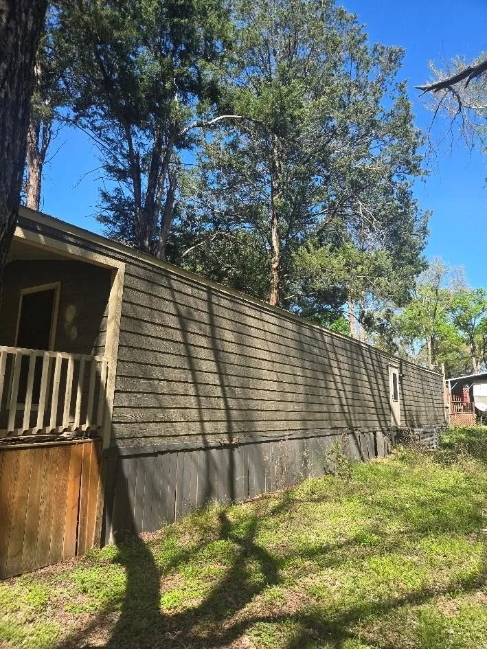 Exterior featuring horizontal siding, a wooden porch railing, and mature trees