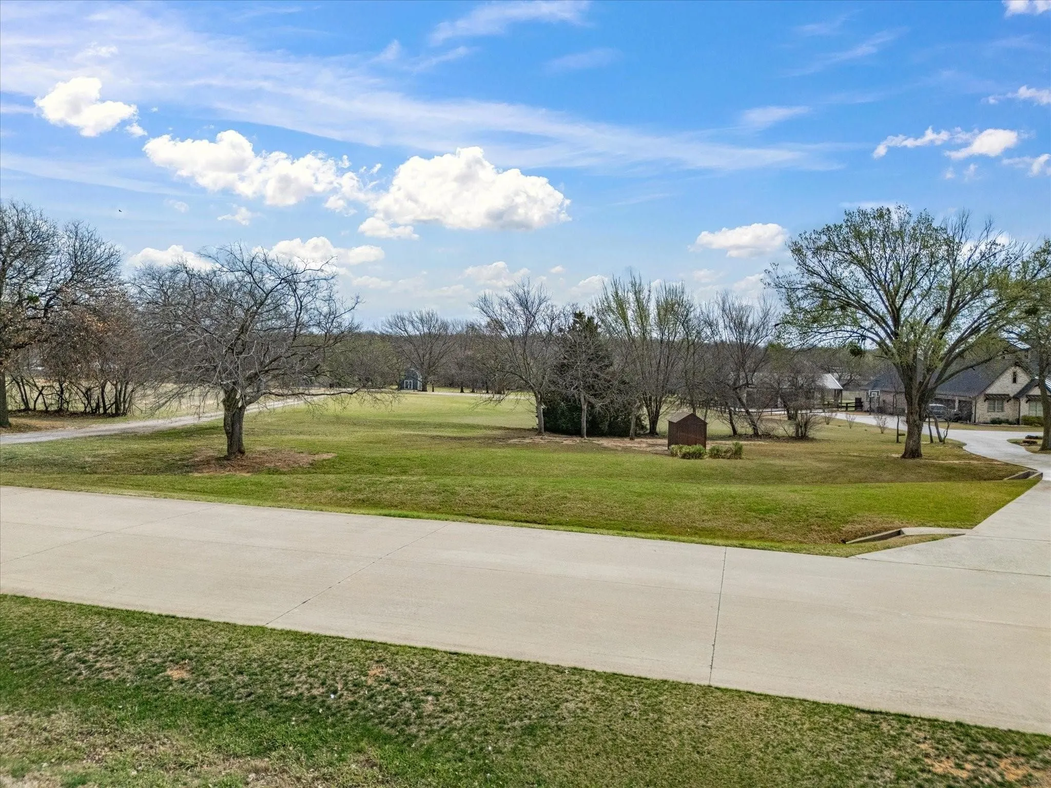 Expansive green space with mature trees and paved road access