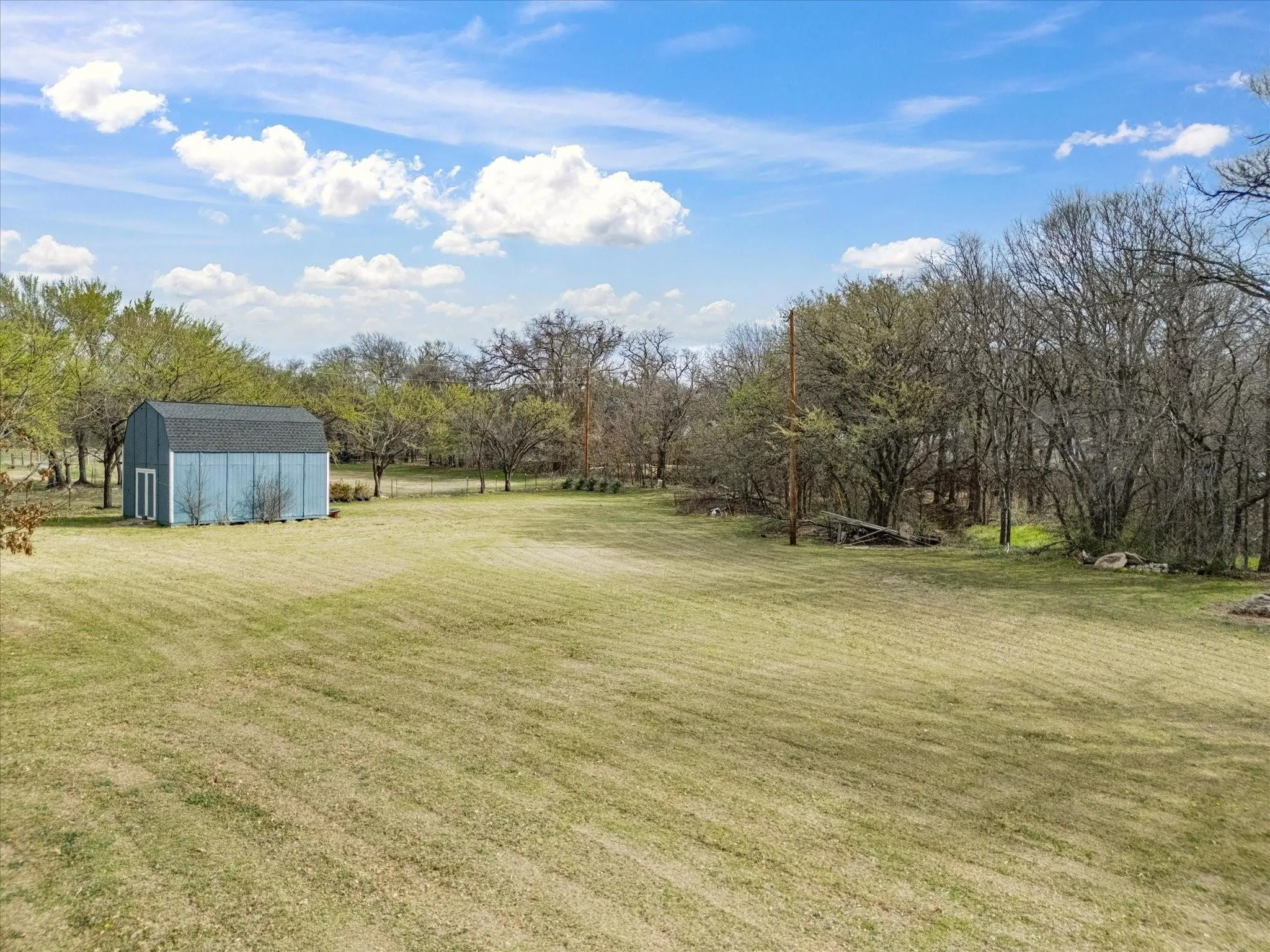 Expansive grassy area with a light blue barn-style shed and surrounding mature trees