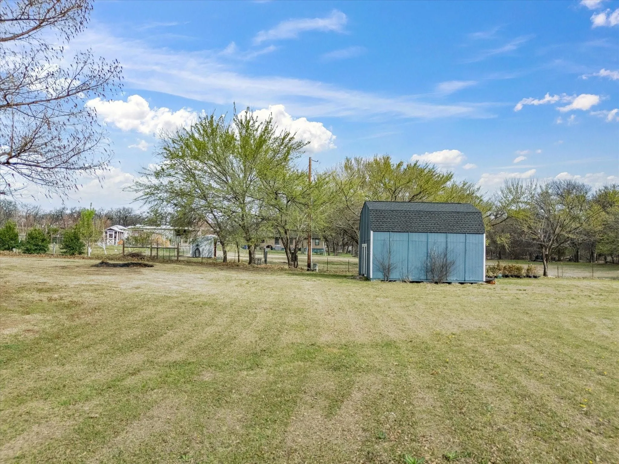 Expansive grassy area with a light blue storage shed featuring a dark shingle roof