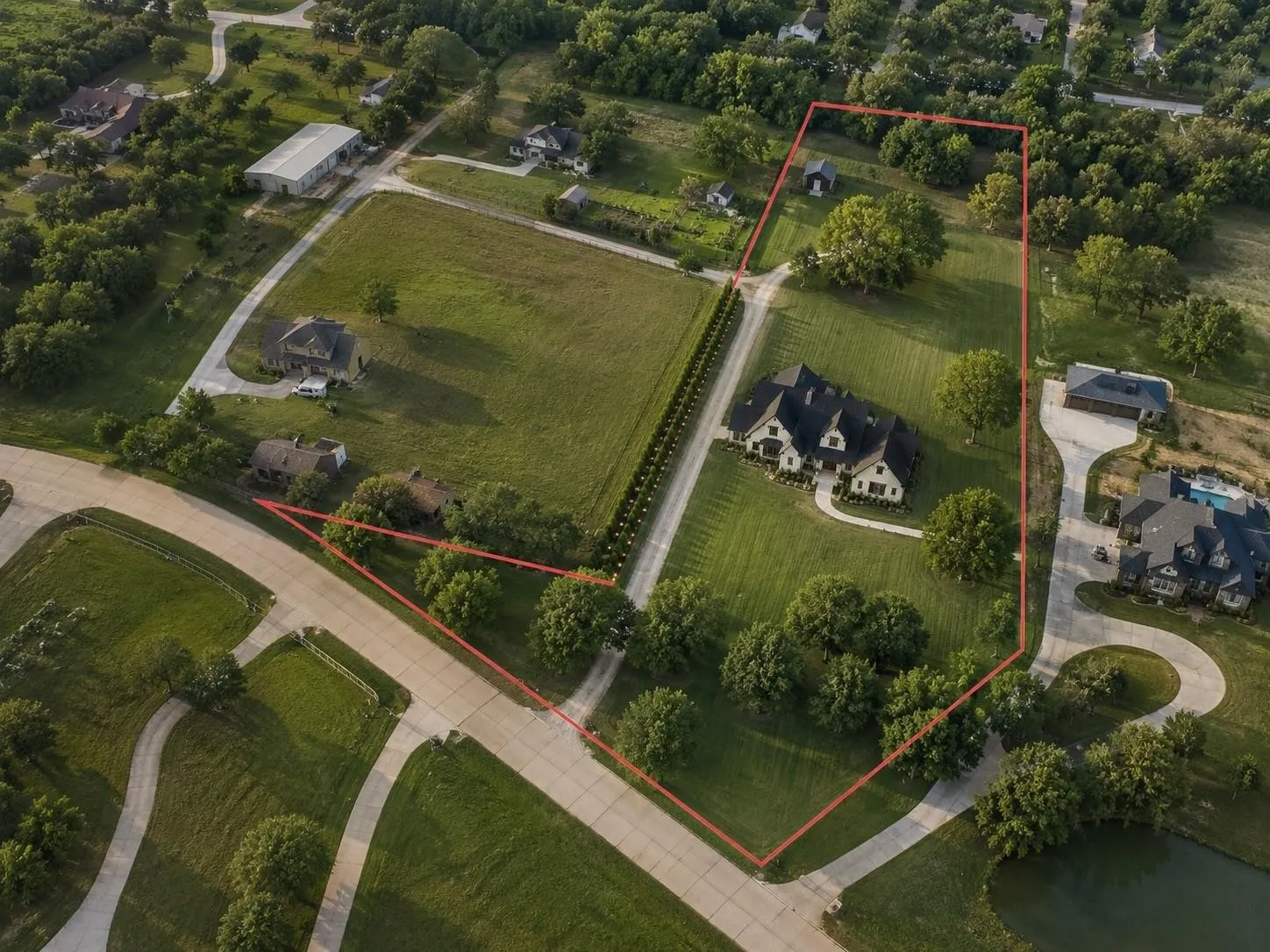 Expansive property featuring a large residence, detached outbuilding, mature trees, manicured lawns, and a private drive
