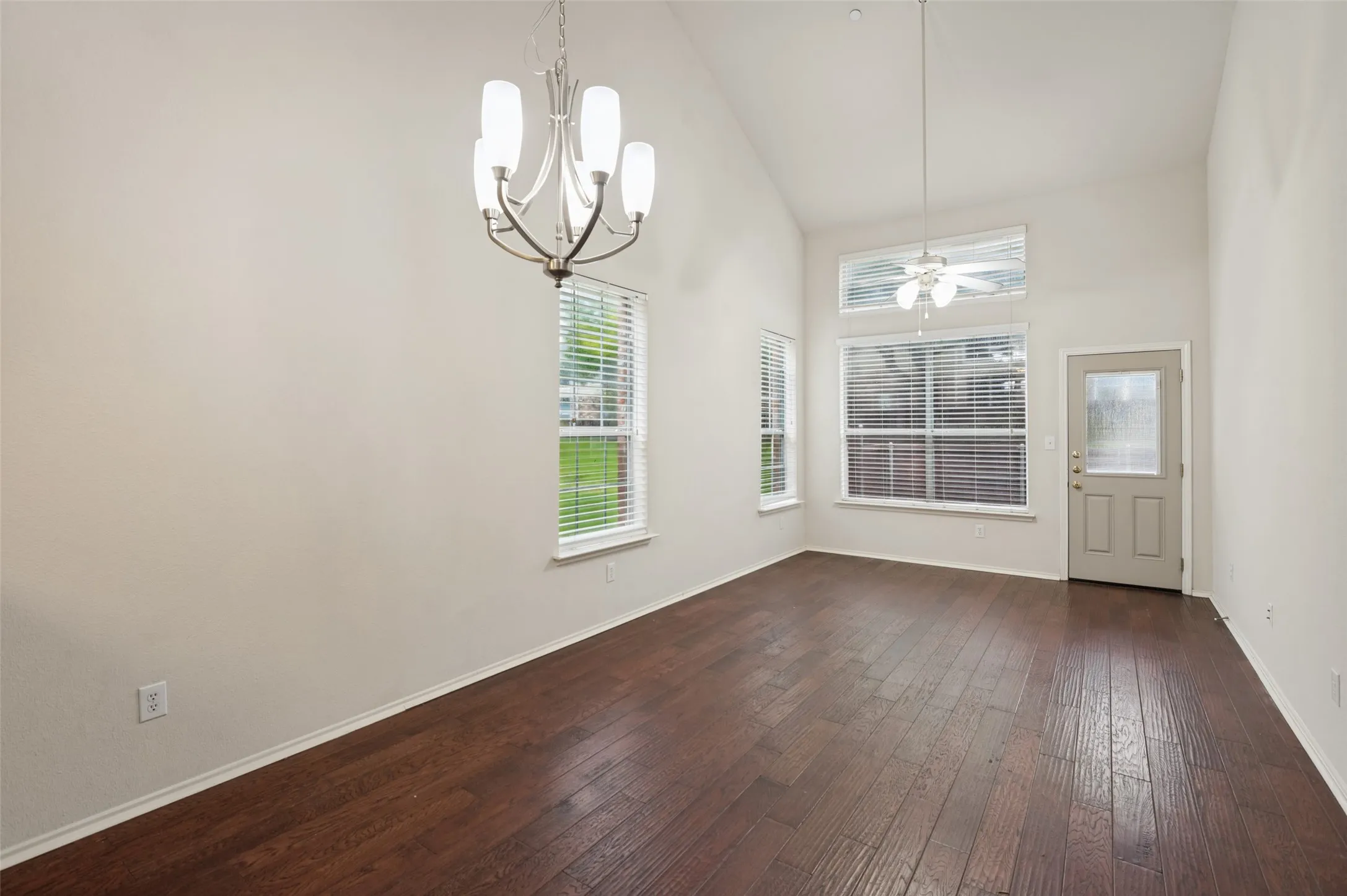 Vaulted ceiling with a chandelier, wood-finish flooring, and multiple windows with blinds