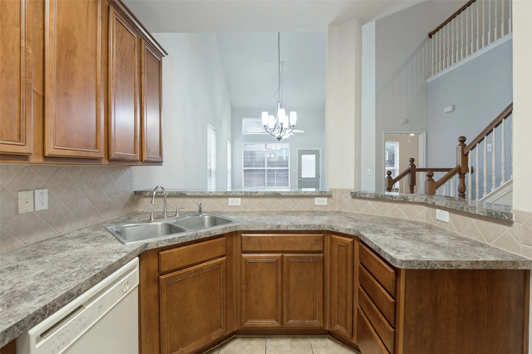Kitchen featuring a double basin sink, ample wood cabinetry, tile backsplash, and durable countertops