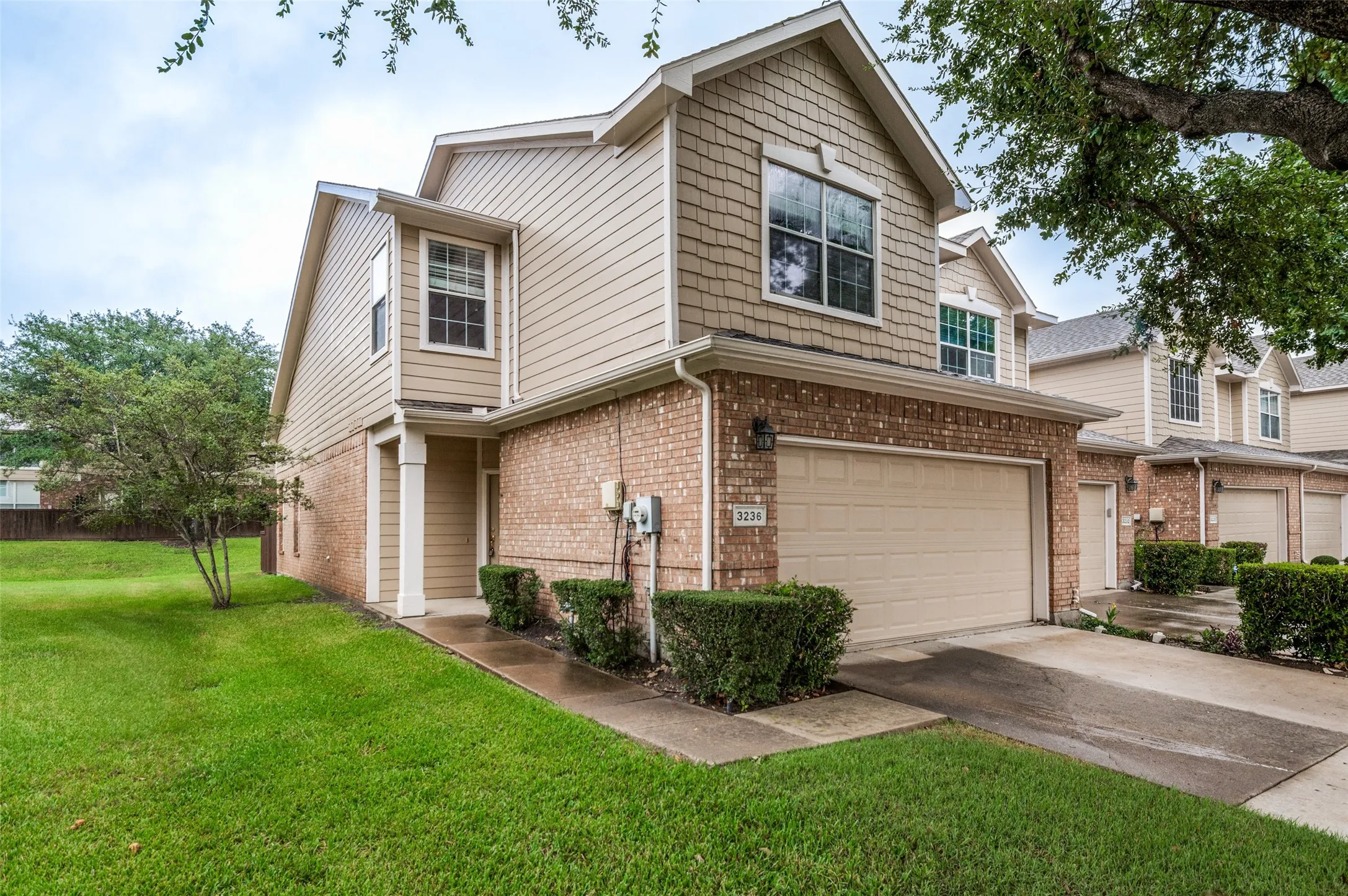 Brick and siding exterior with shake accents, featuring an attached garage, covered entry, and landscaped shrubbery