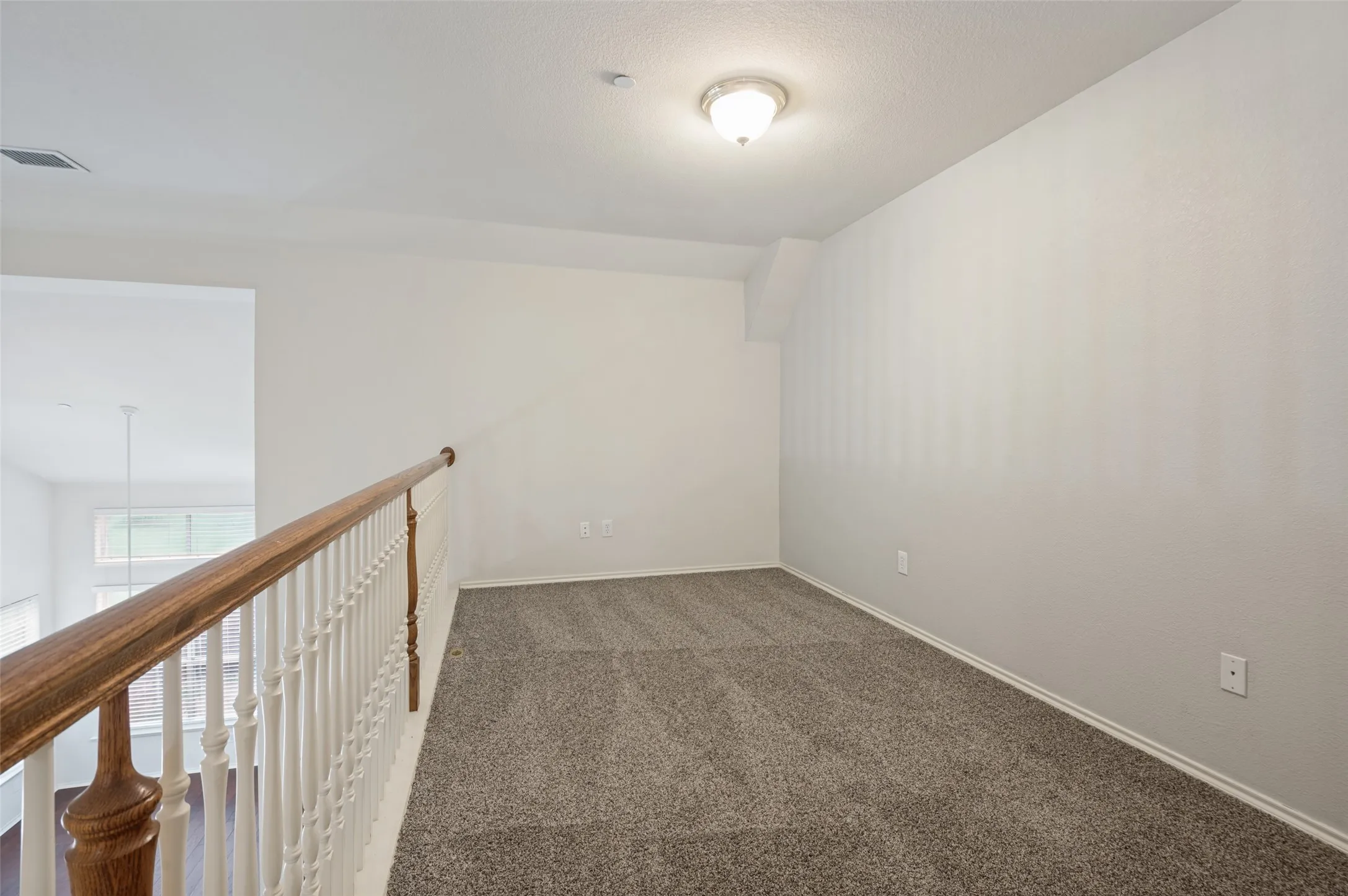 Carpeted loft area with a wood handrail, white balusters, and a semi-flush mount light fixture