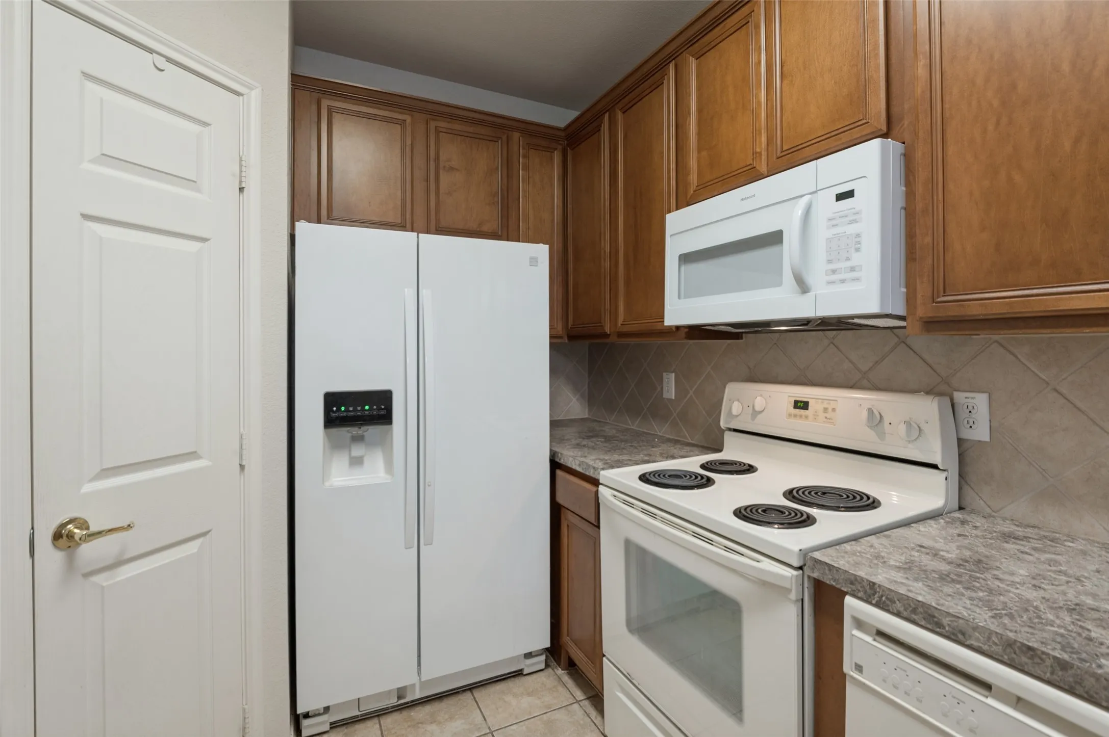 Wood-finish cabinetry, tile backsplash, white appliances, and a built-in microwave