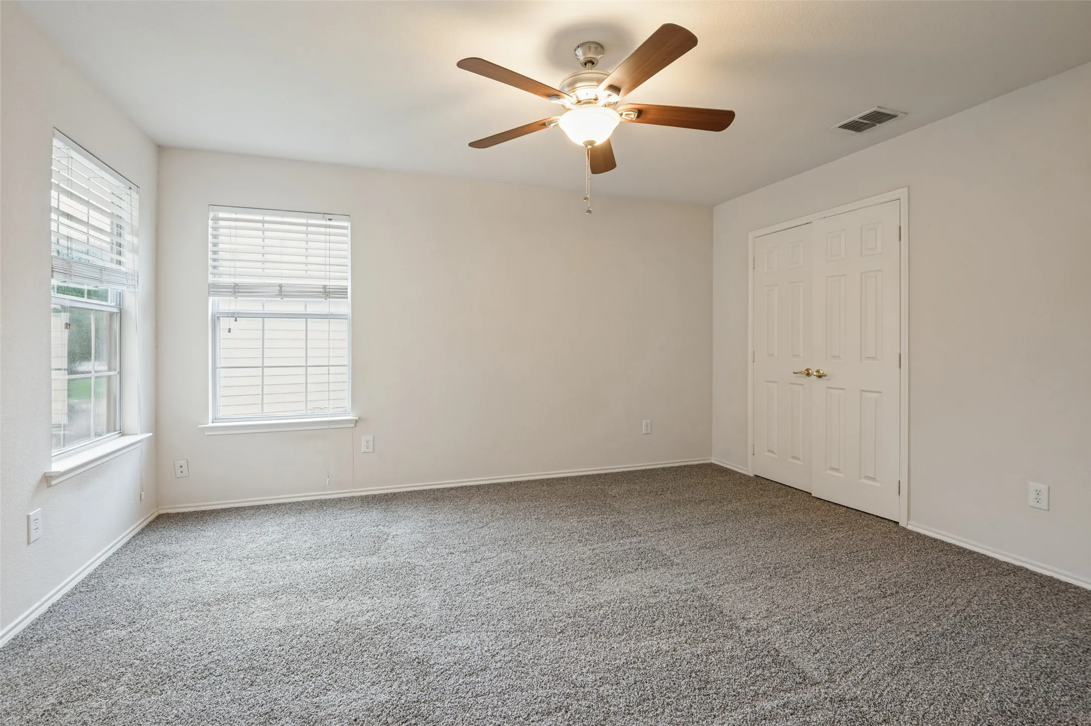 Carpeted room with a ceiling fan, two windows with blinds, and white paneled bi-fold doors