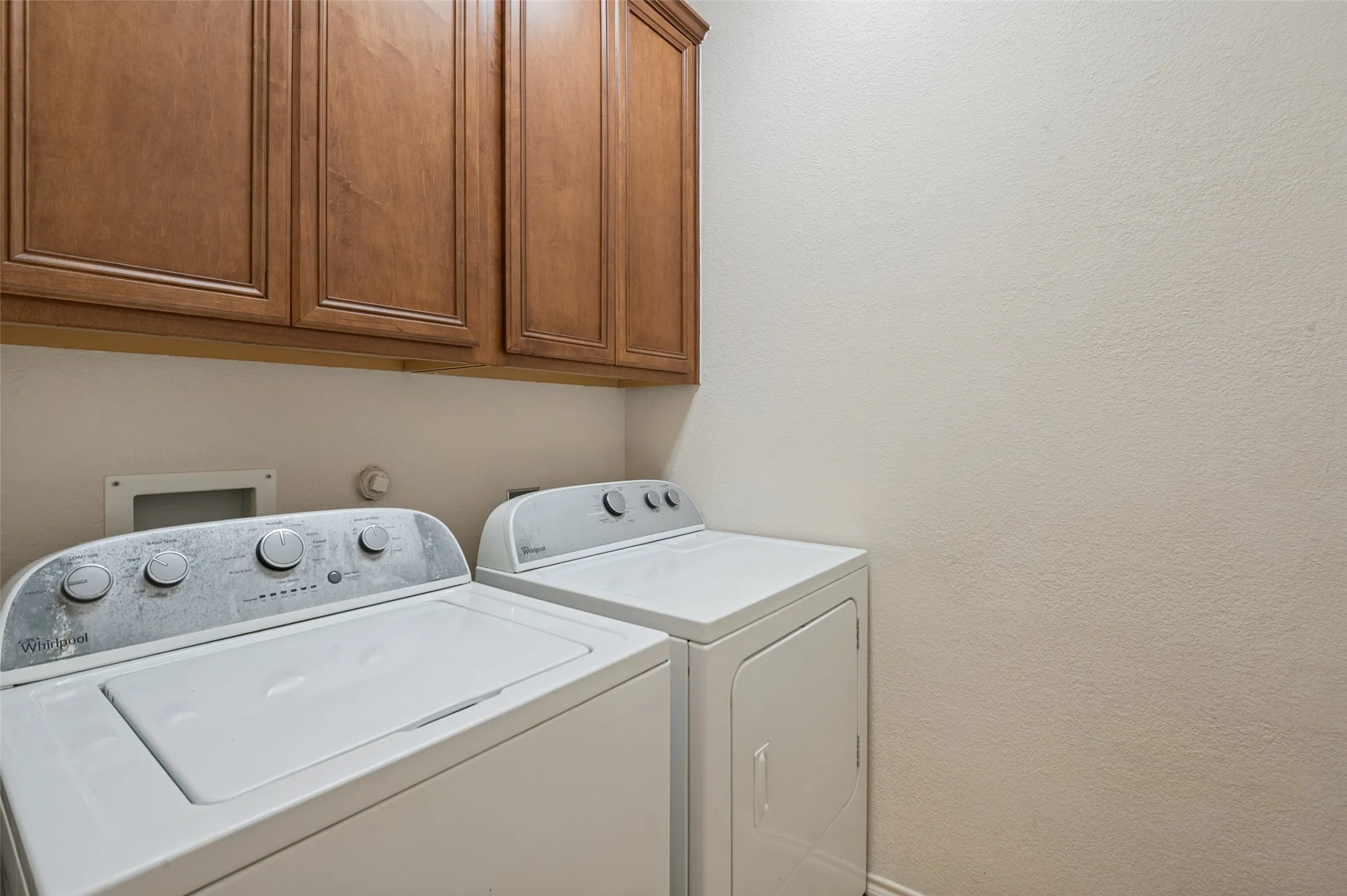 White washer and dryer appliances, wood-finish cabinetry, and neutral wall tones