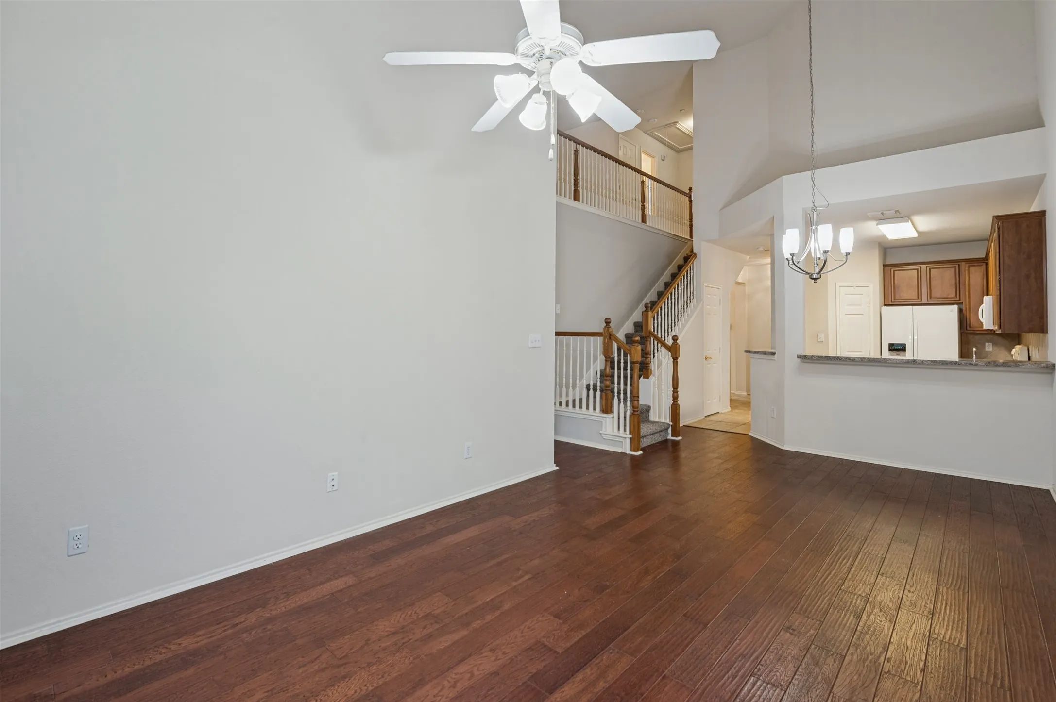 High ceilings with a ceiling fan, wood-finish flooring, staircase with wood newel posts, kitchen featuring wood cabinetry, and a breakfast bar with a stone-finish countertop