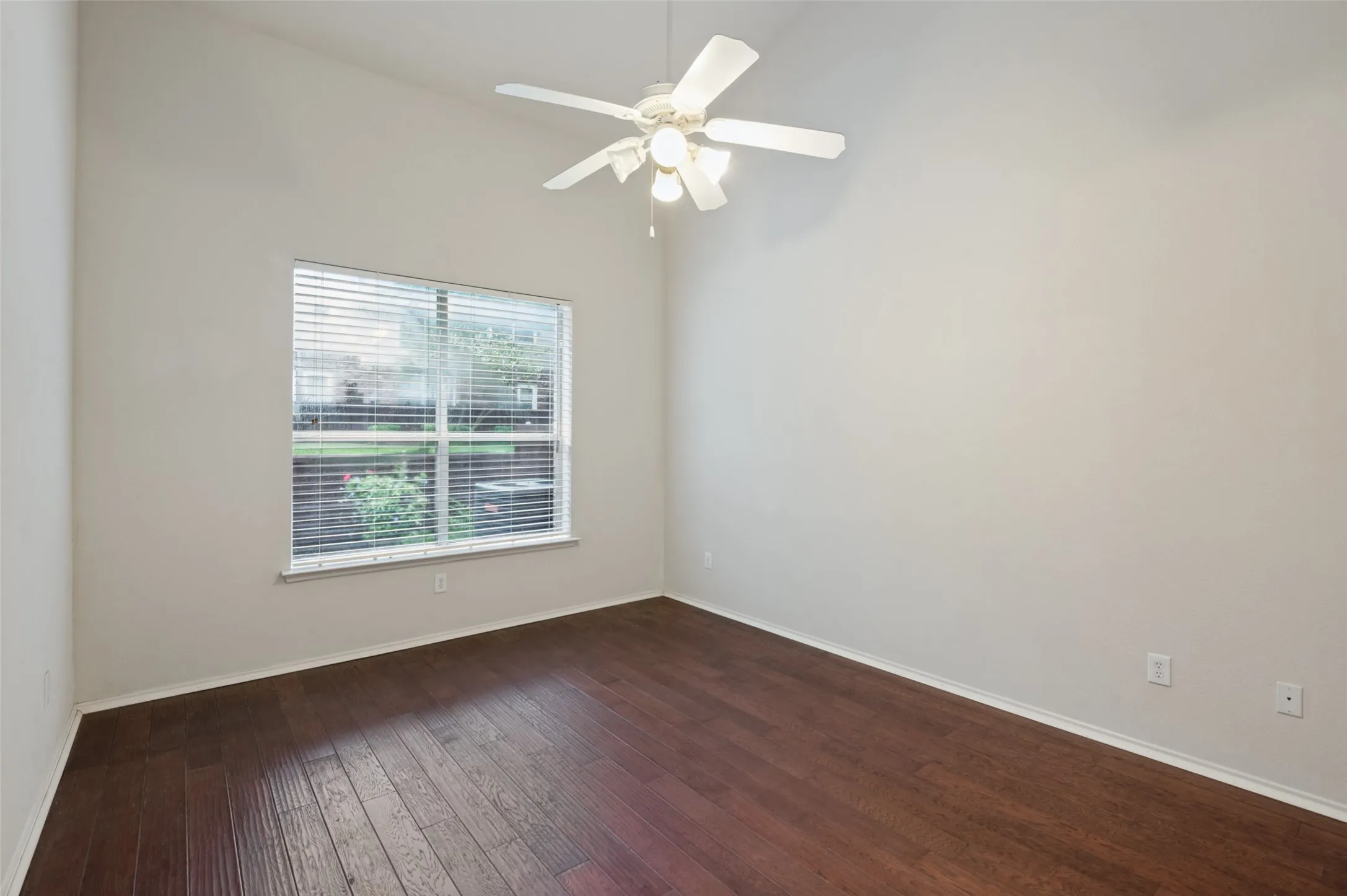 Vaulted ceiling, wood-finish flooring, ceiling fan with integrated lighting, and a large window with blinds