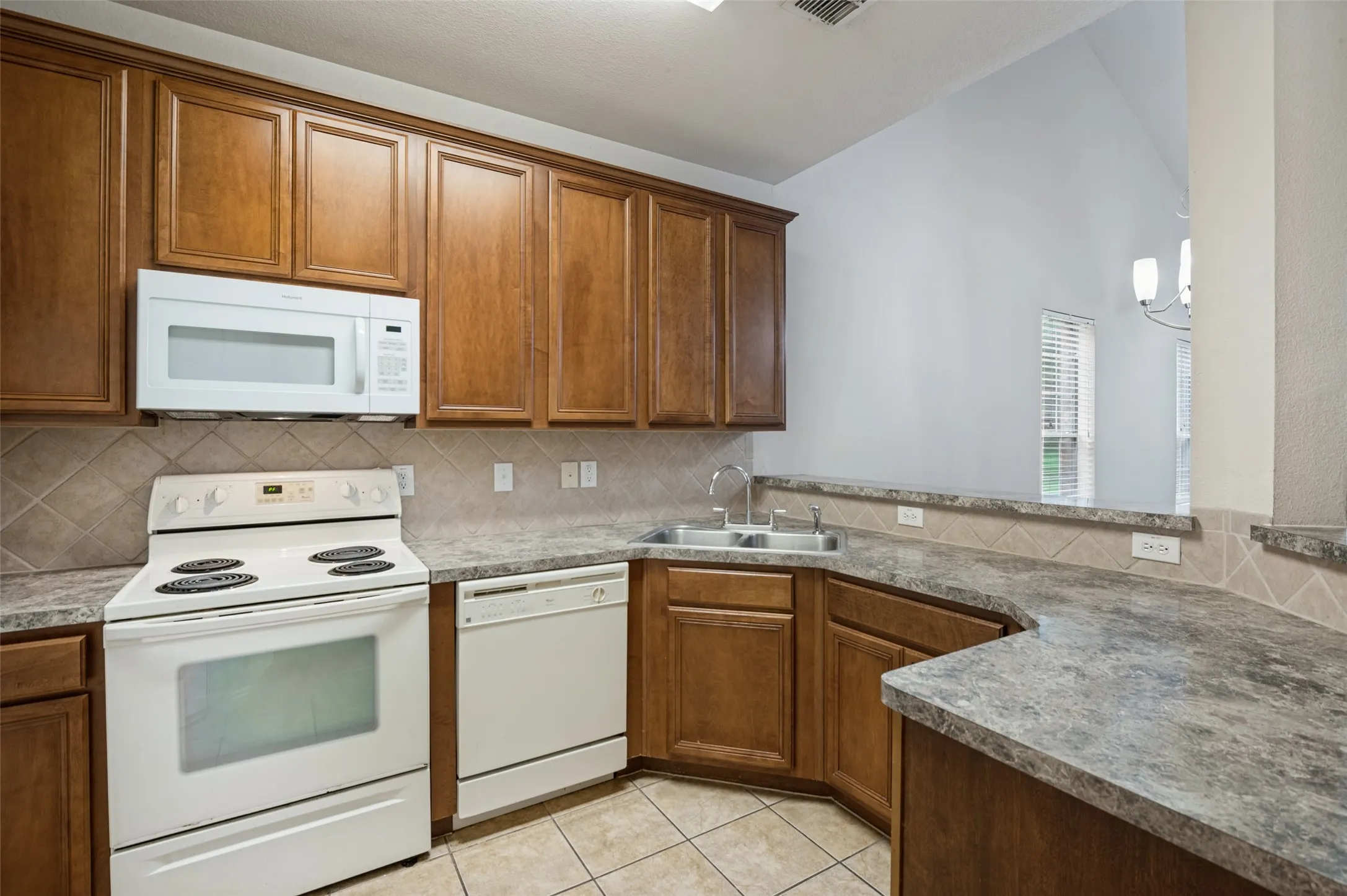 Kitchen featuring wood cabinetry, solid surface countertops, white appliances, and a tiled backsplash