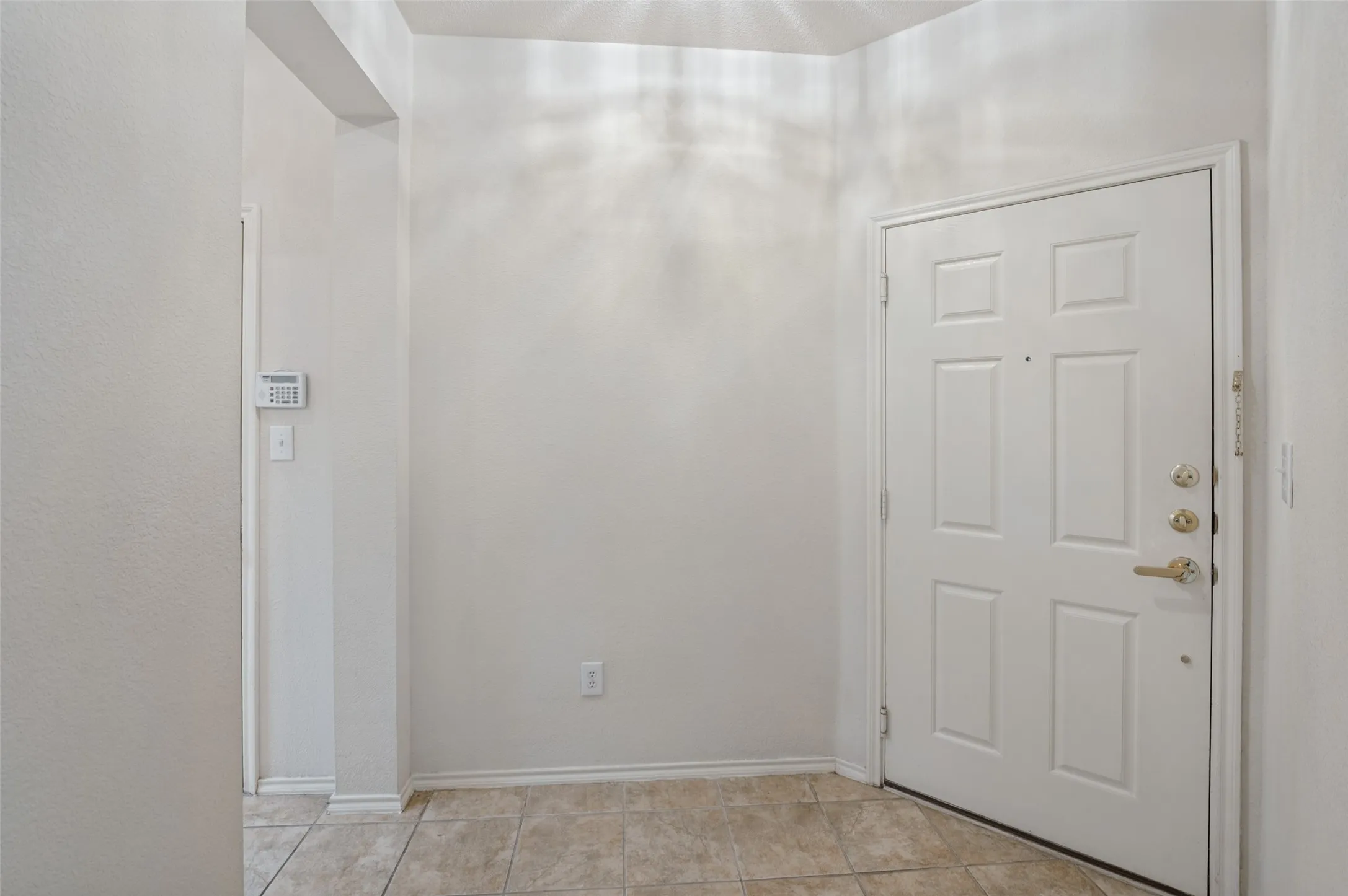 White paneled door with brass hardware, light-toned tile flooring, and neutral wall tones