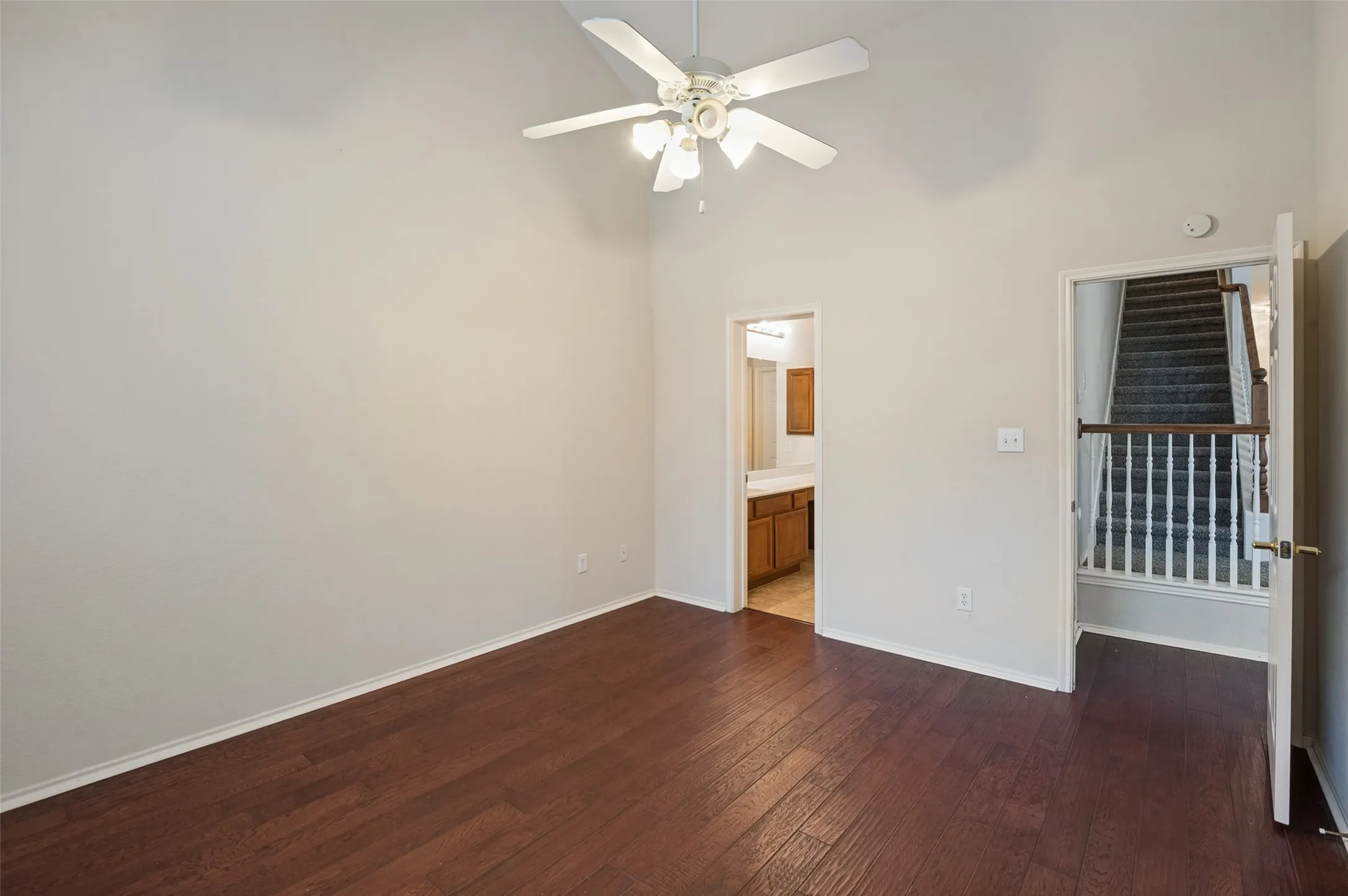 Vaulted ceiling with a ceiling fan, wood-finish flooring, and direct access to a bathroom with a vanity