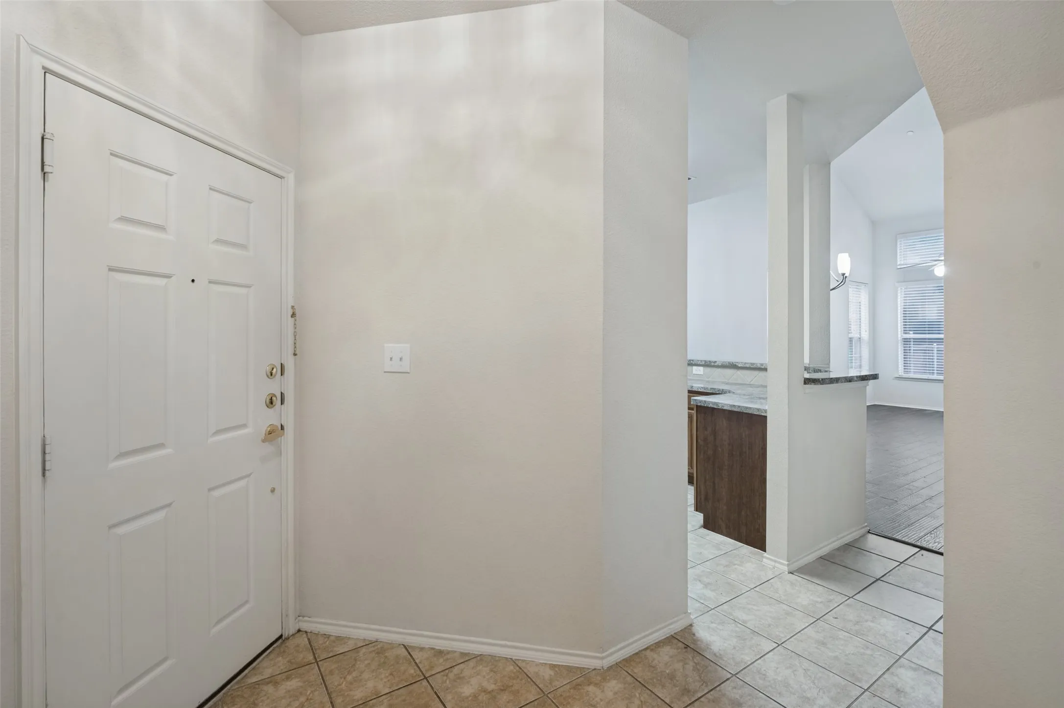 Panel-style entry door, tile flooring, granite-look countertop, wood-finish cabinetry, and vaulted ceiling