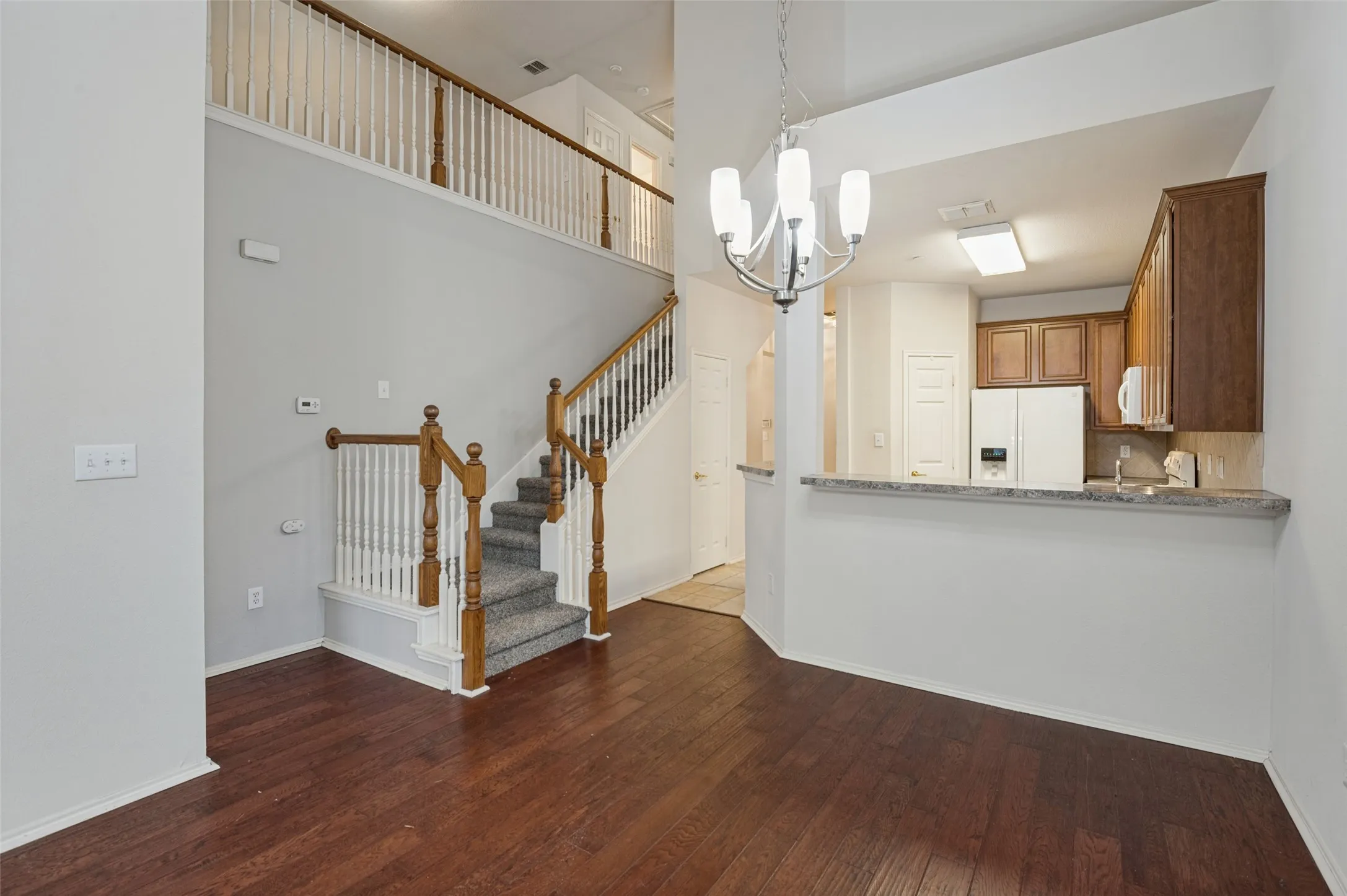 Dark wood-finish flooring, staircase with wood banister and carpeted treads, and a kitchen pass-through with stone-look countertop