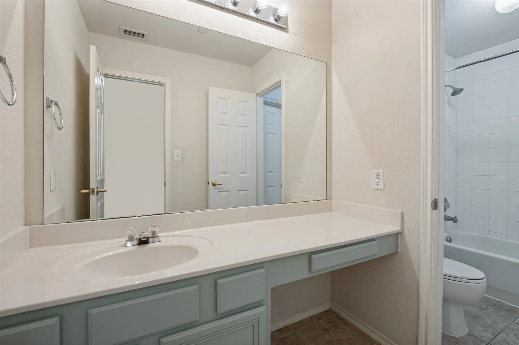 Vanity with an integrated sink and light blue cabinetry, chrome faucet, expansive wall-mounted mirror, and overhead vanity lighting
