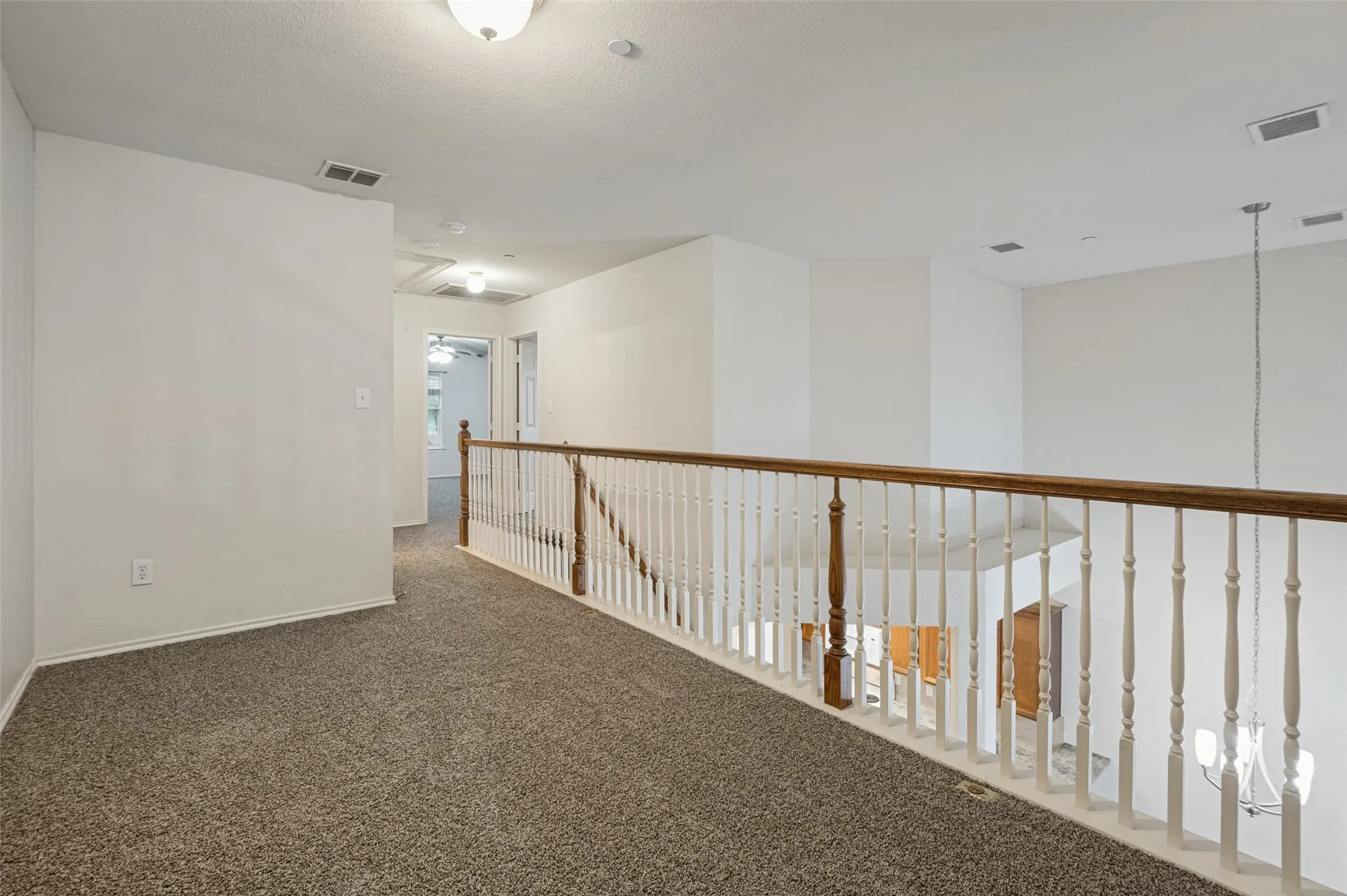 Carpeted loft area featuring a wood-finish handrail and painted balusters