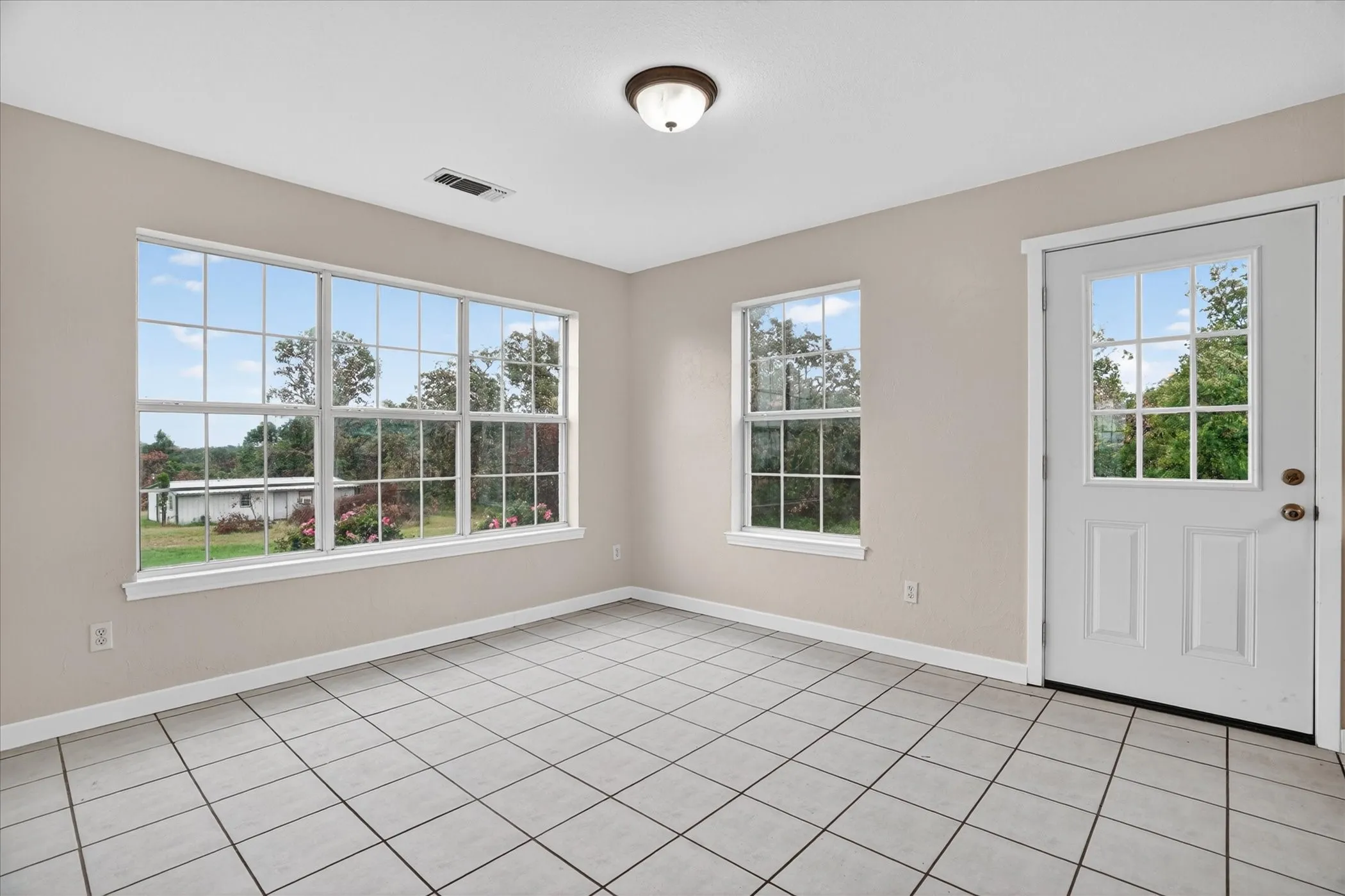 White tiled flooring, neutral wall tones, multiple large pane windows, and a panel door with integrated window