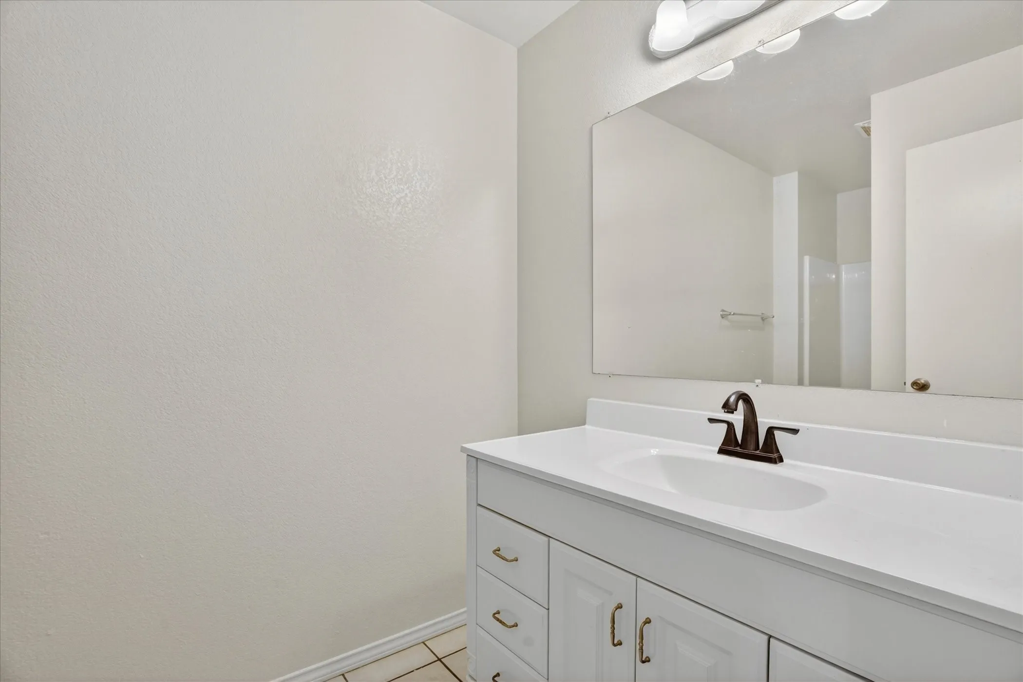 White vanity with a single basin sink, bronze-finish faucet, and a large wall-mounted mirror