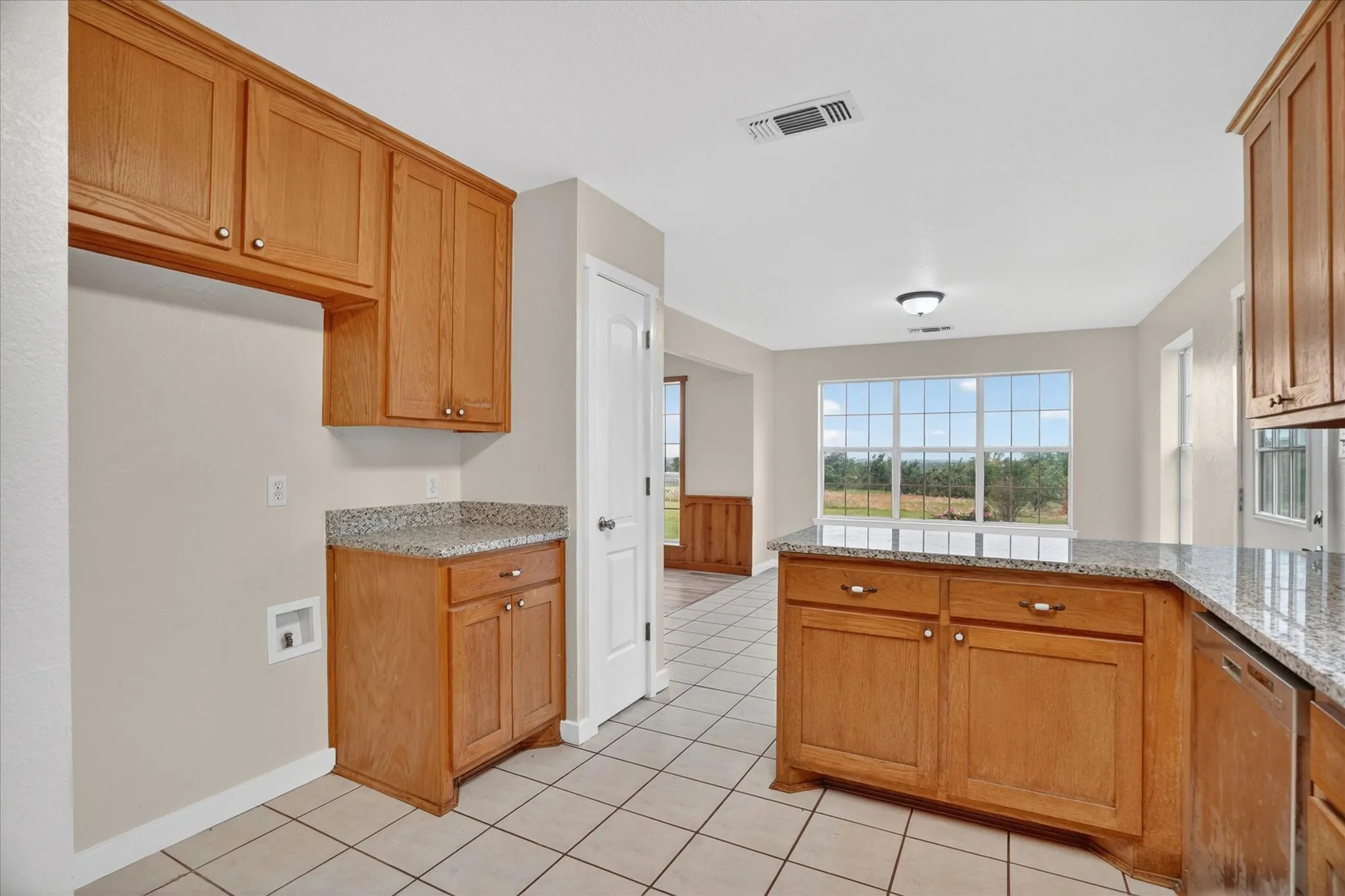 Kitchen with wood cabinetry, light-toned countertop, tile flooring, and a large window overlooking natural scenery