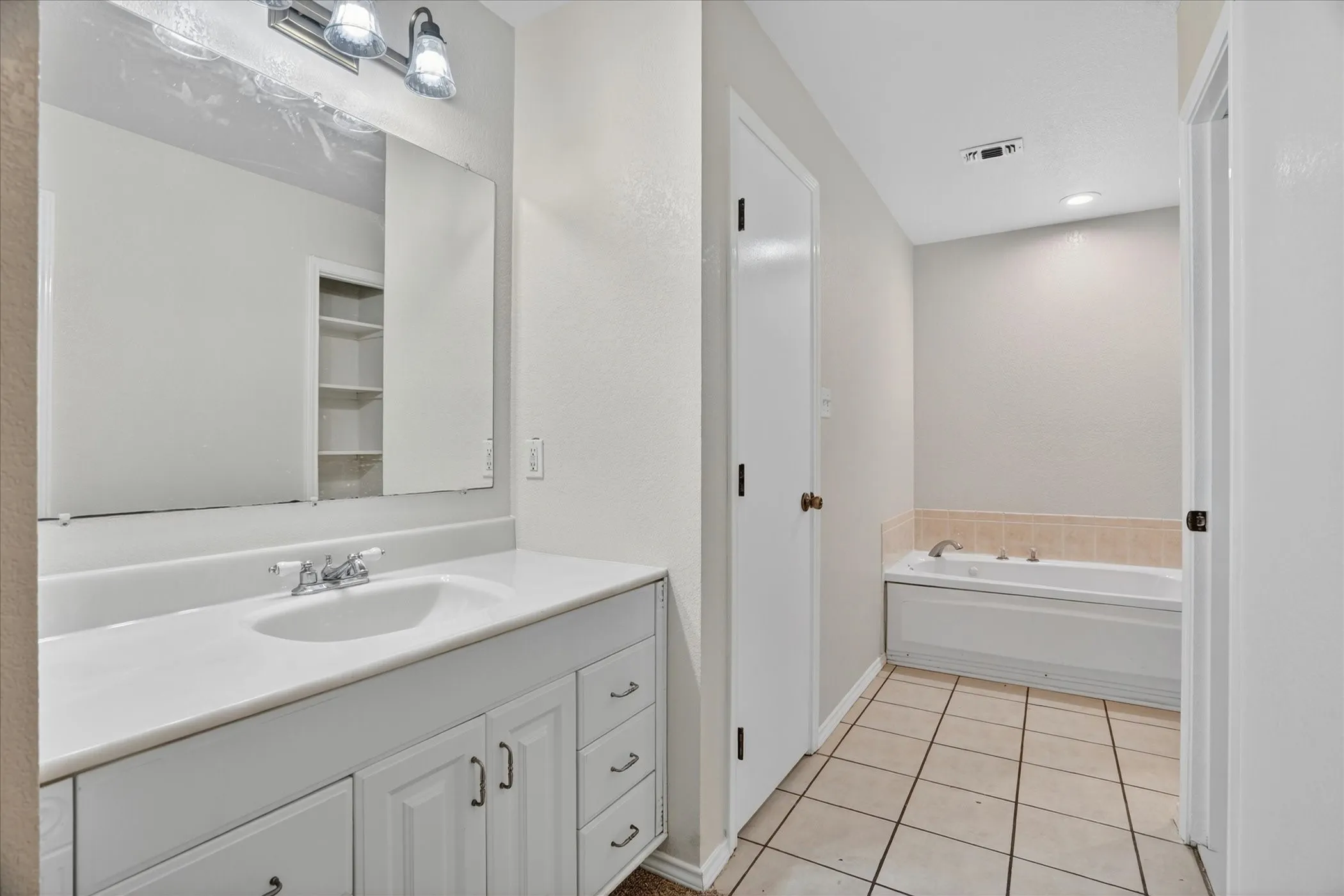 Bathroom featuring a single vanity with storage, an integrated sink, a built-in tub with tile surround, and square floor tiles