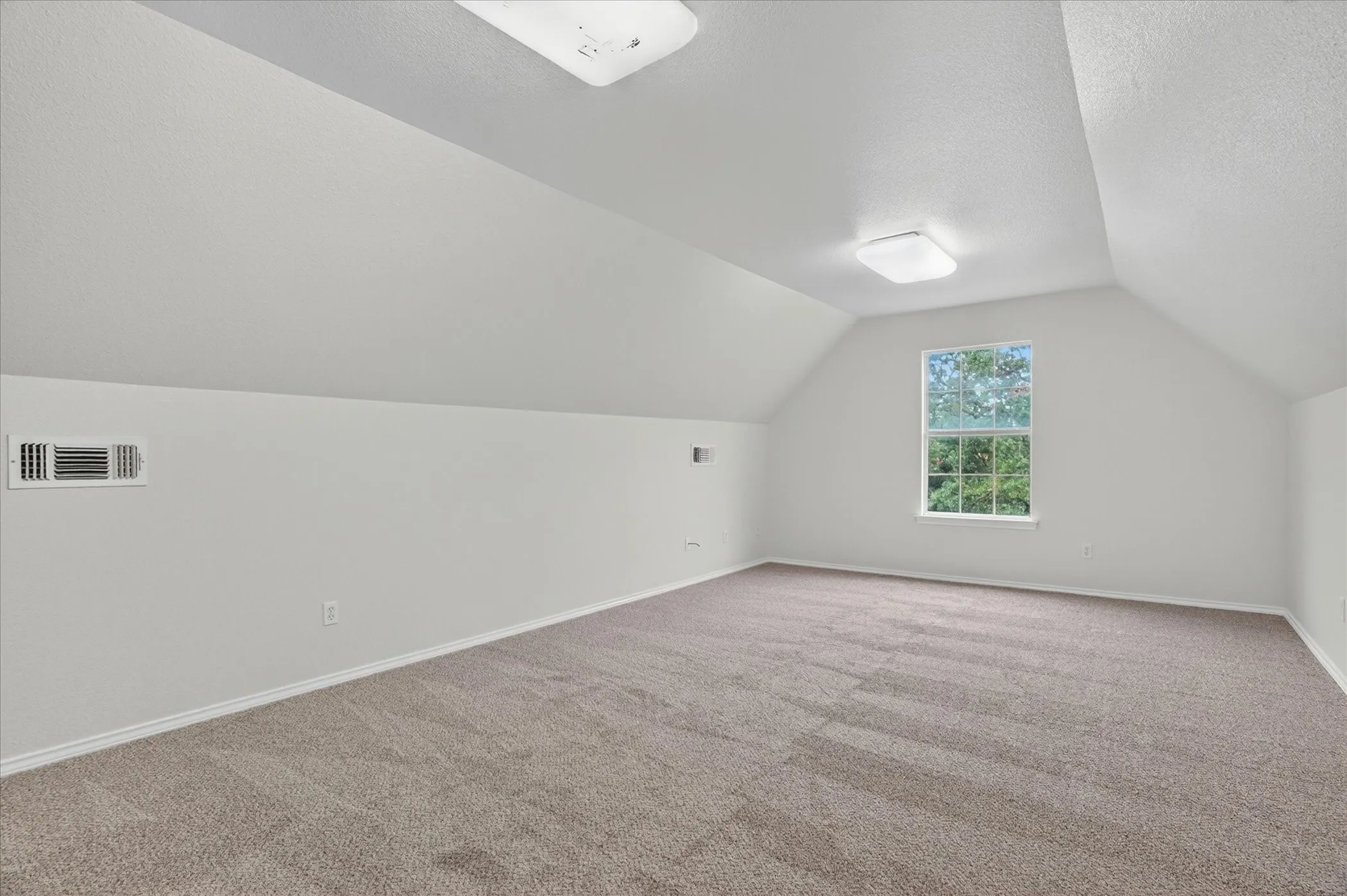 Spacious room featuring vaulted ceilings, neutral-toned carpeting, and a window with exterior visibility